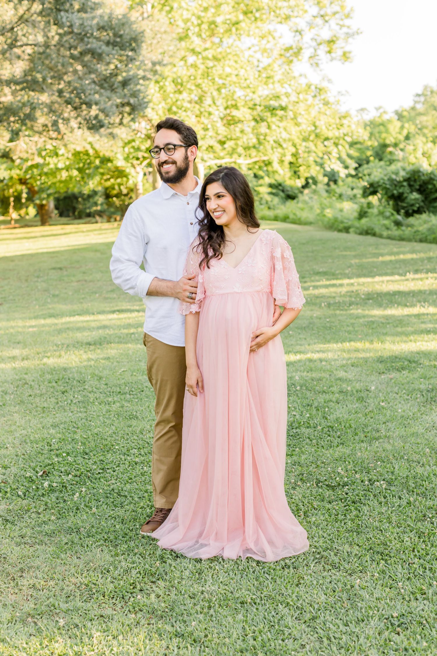 Happy couple poses together outdoors with woman wearing pink empire waist maternity gown.