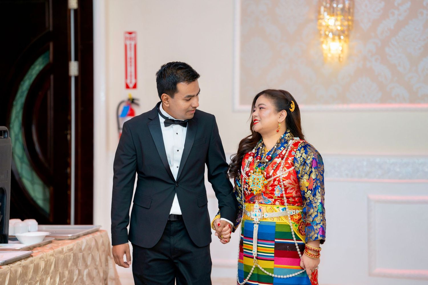A couple shares a happy moment in formal wear, with traditional colorful dress contrasting a black tuxedo.