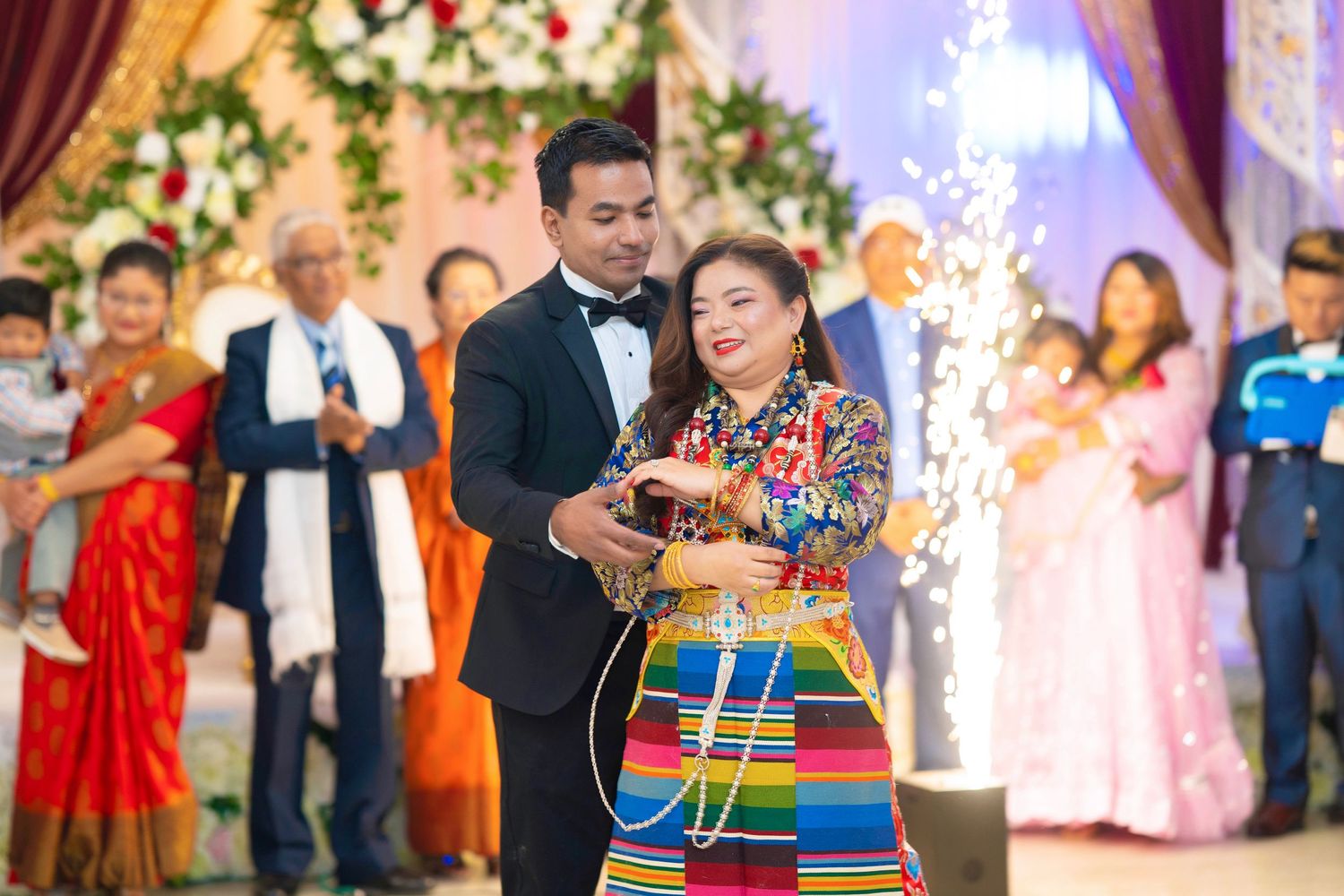 A couple celebrates a special moment surrounded by guests at an ornate indoor venue.