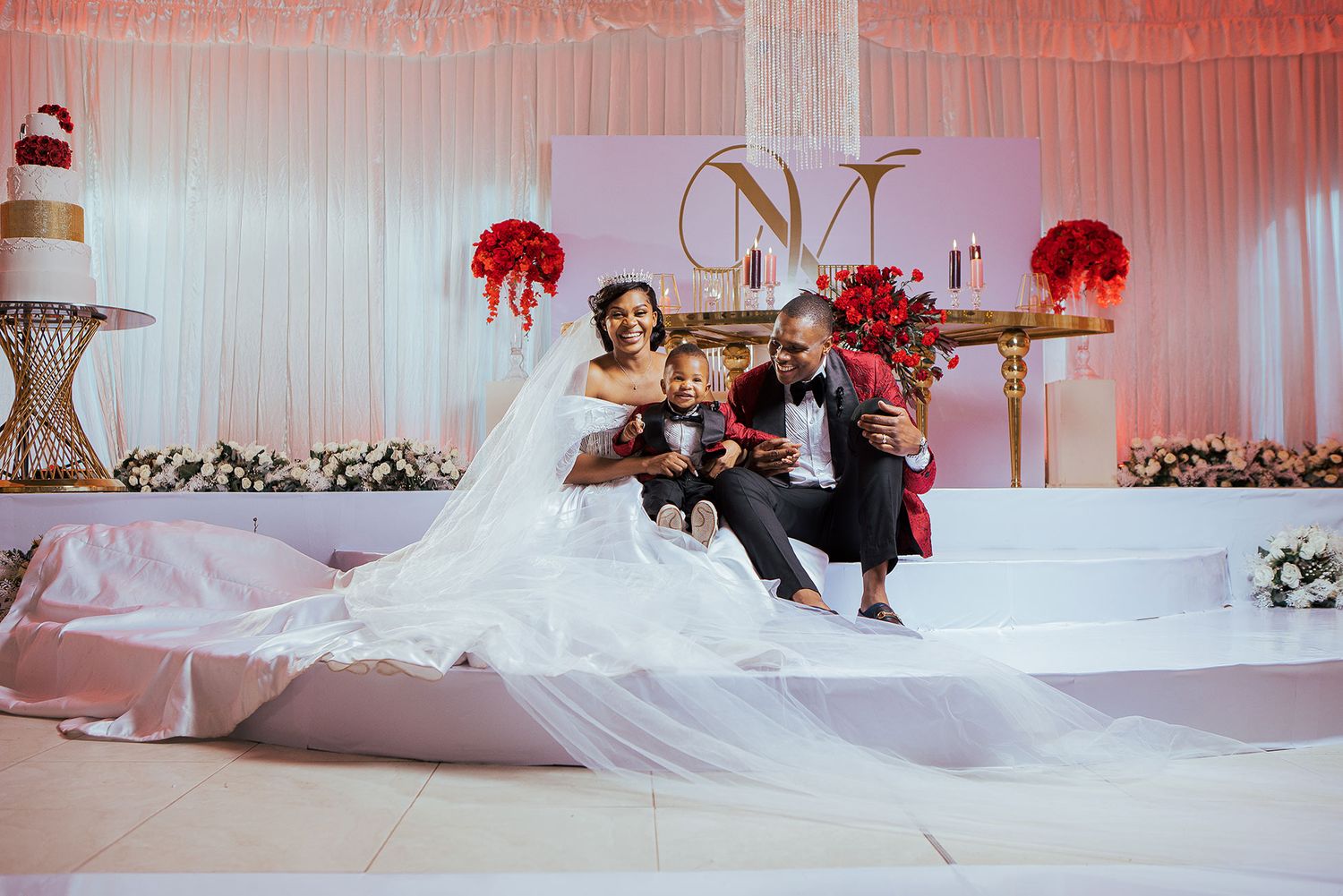 Elegant wedding reception setup with red floral arrangements and white backdrop decor.