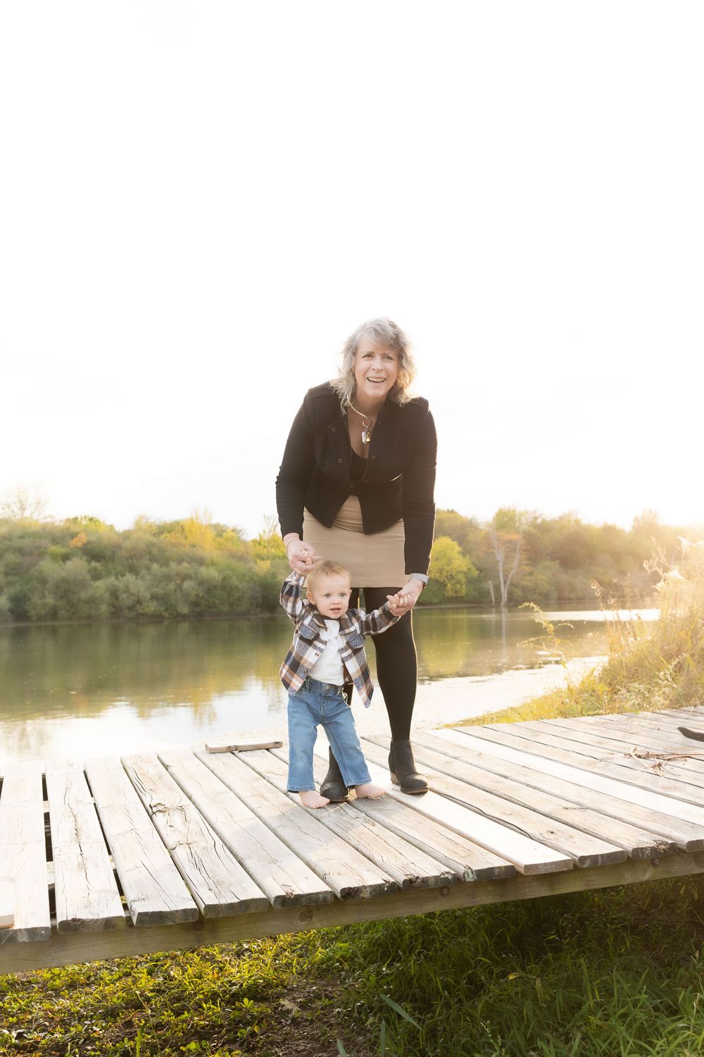 Two people stand together on a wooden dock by a serene lake at sunset.