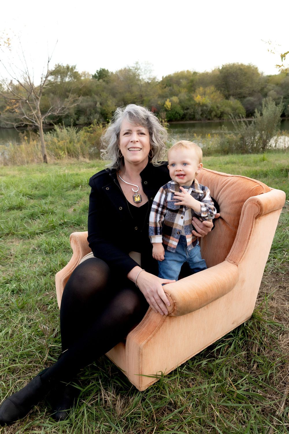 Two people sit together on a vintage tan leather chair in a grassy meadow.