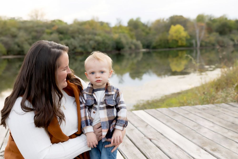 Two people share a moment sitting on a wooden dock by a peaceful lake.