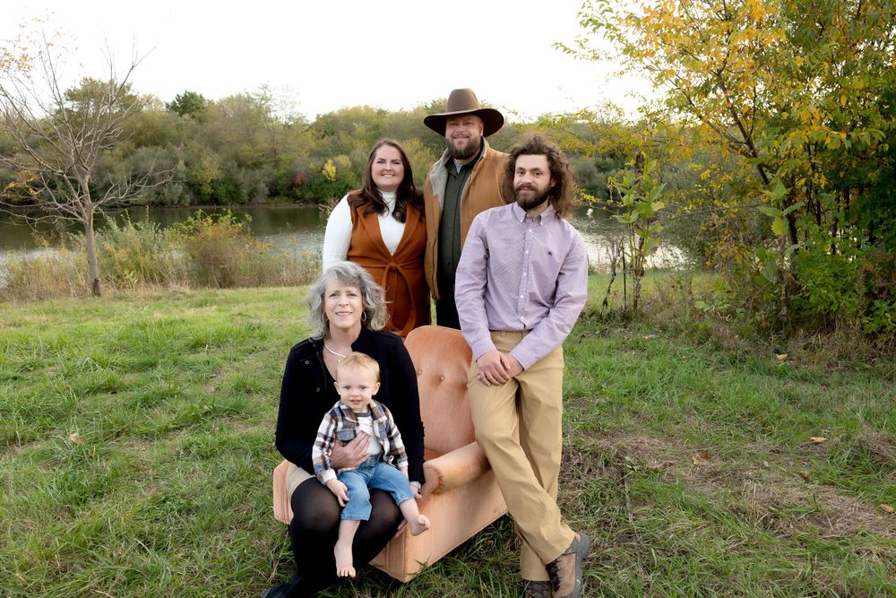 Group poses casually together in outdoor setting with lake and trees in background.