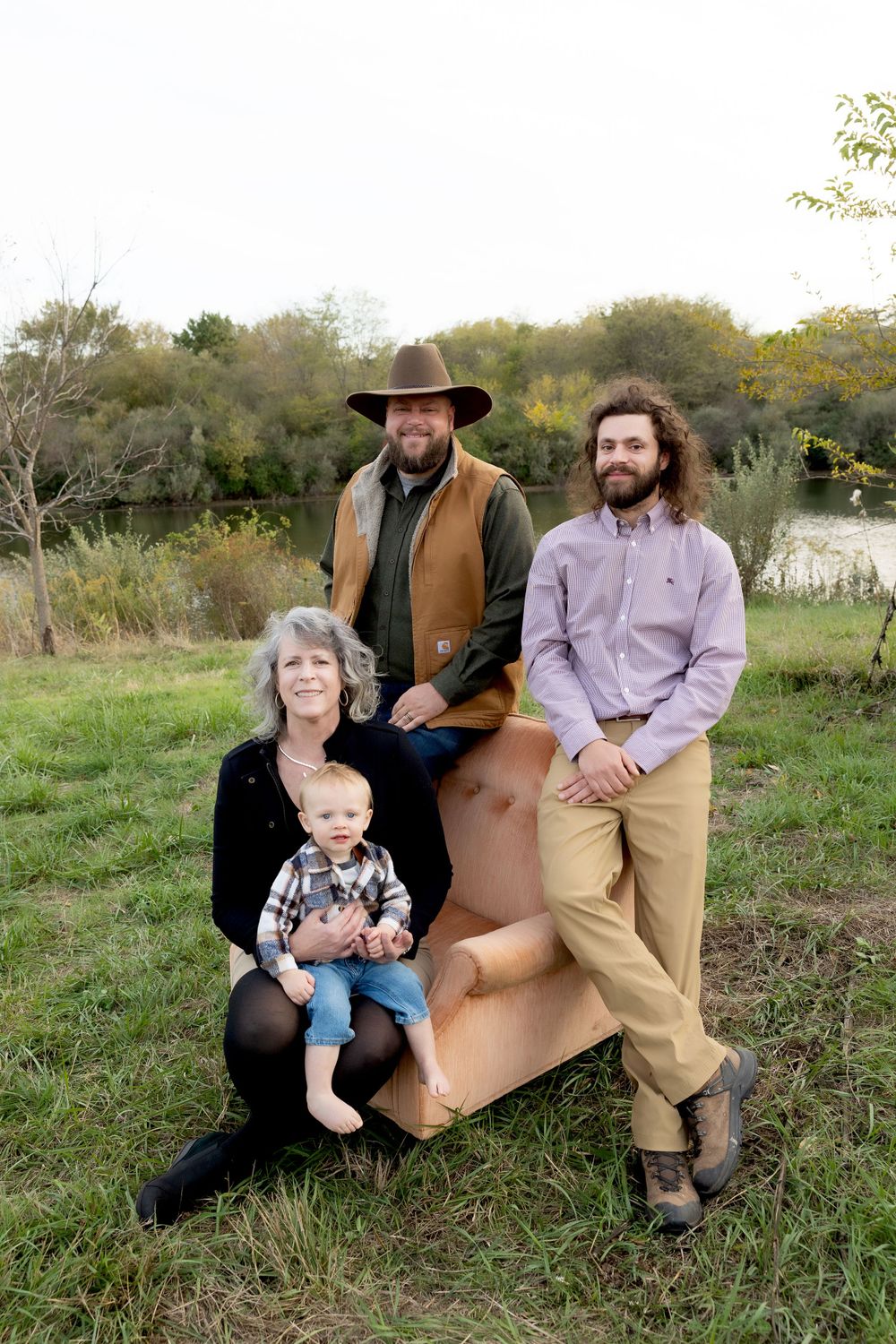 Family poses together on a tan leather chair outdoors in a natural setting.