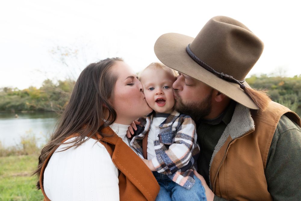 Family shares tender moment outdoors near a lake during golden hour.