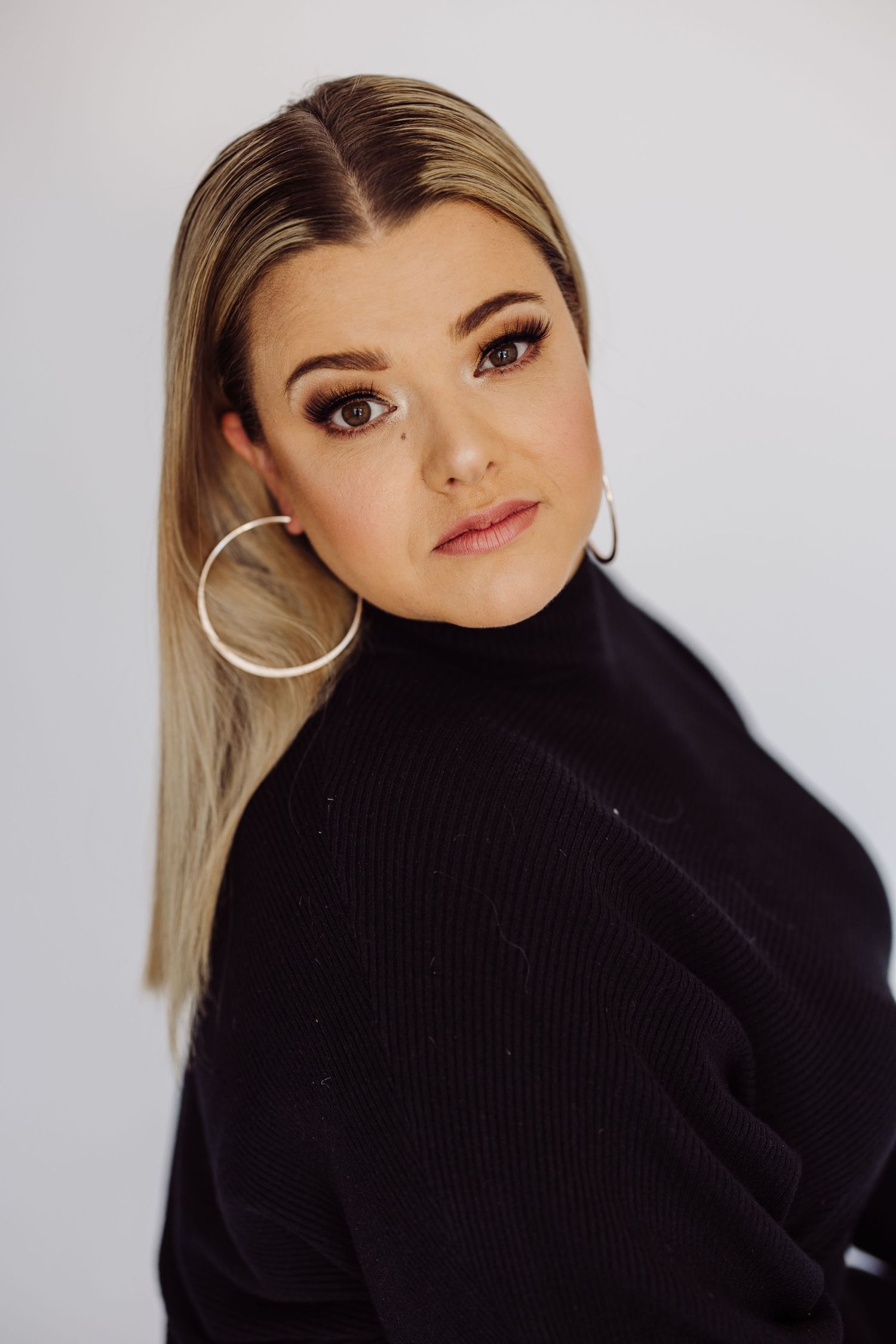 Studio portrait with black turtleneck sweater and large hoop earrings against white background.