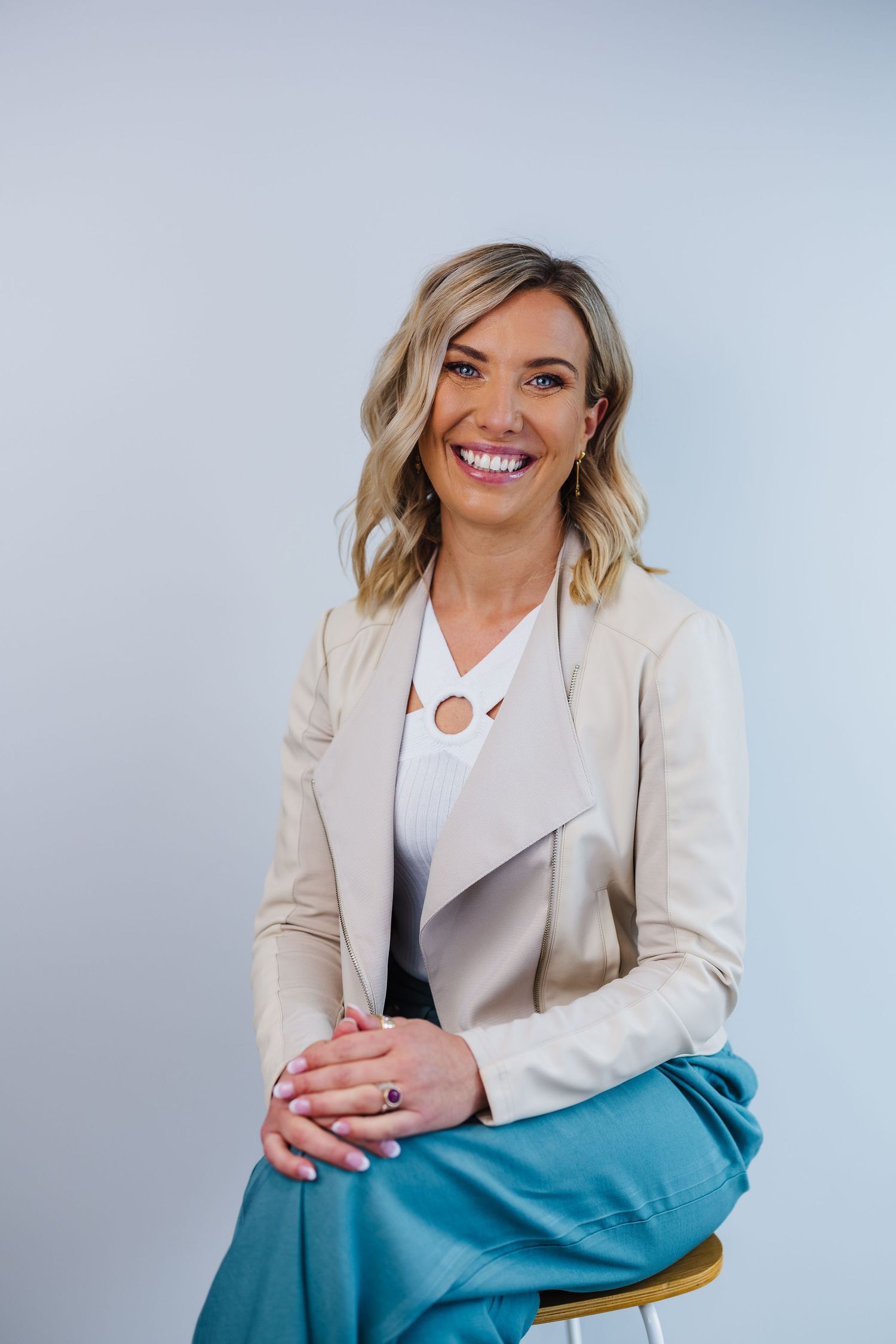 Professional in cream blazer and teal skirt sitting against light background.