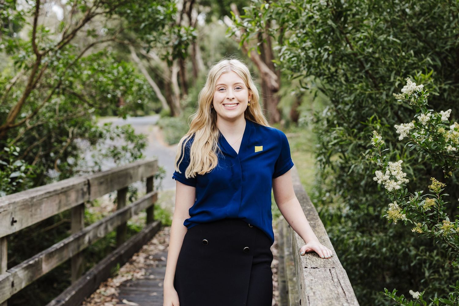 Professional in navy polo shirt standing on wooden bridge surrounded by greenery.