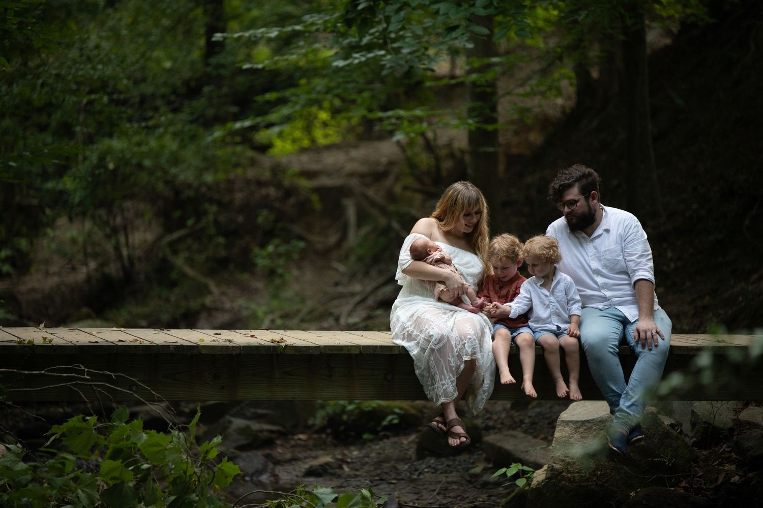 Family sitting together on stone steps near a serene pond in a lush forest setting.