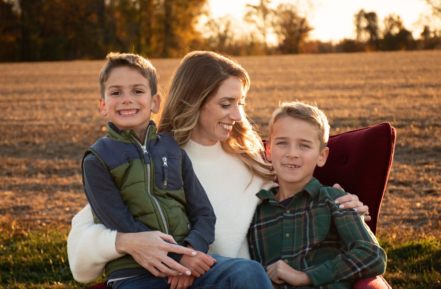 Three people share a warm embrace while sitting together in a sunlit autumn field.