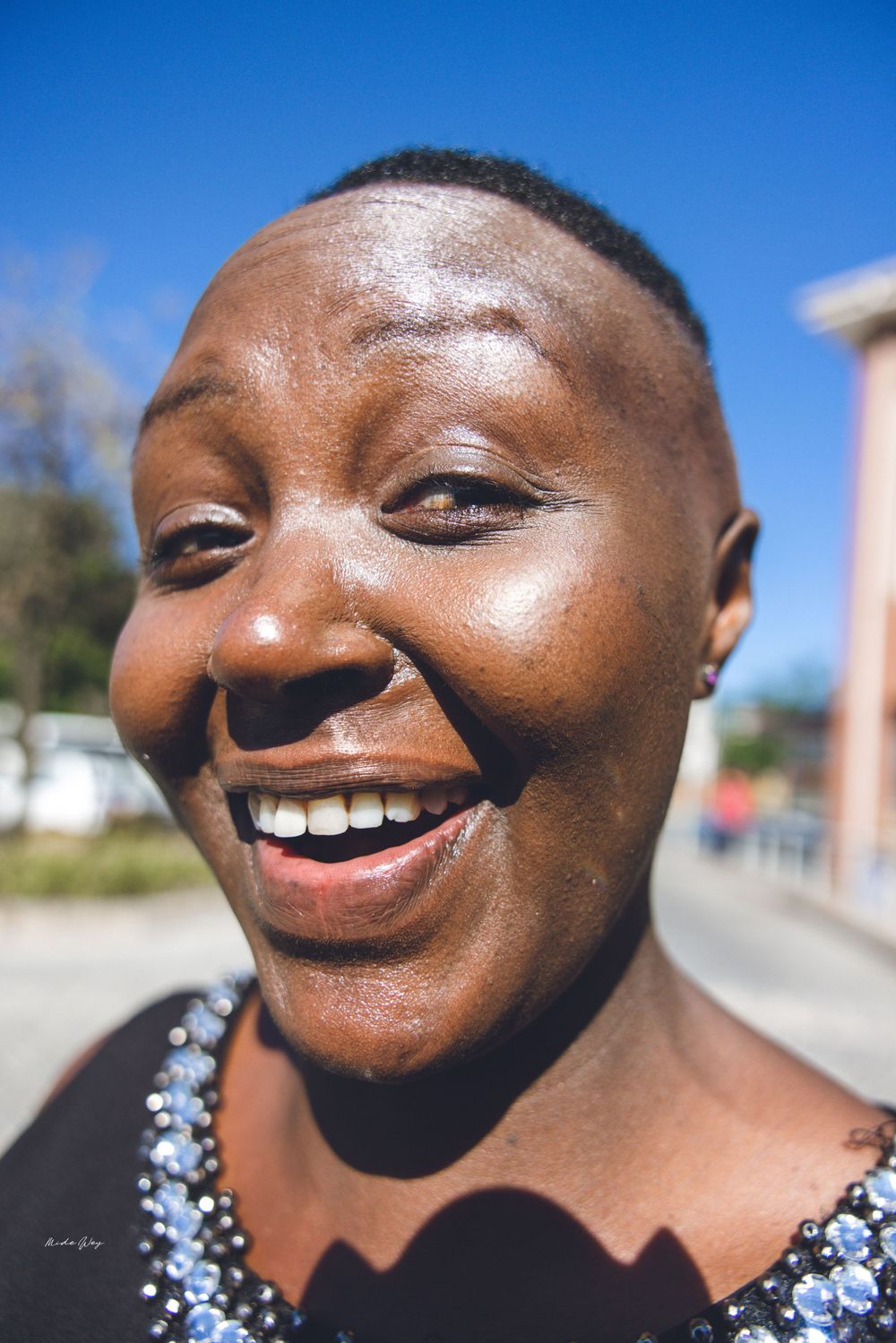 Close up portrait of someone with short hair laughing joyfully in bright sunlight wearing a sequined top.