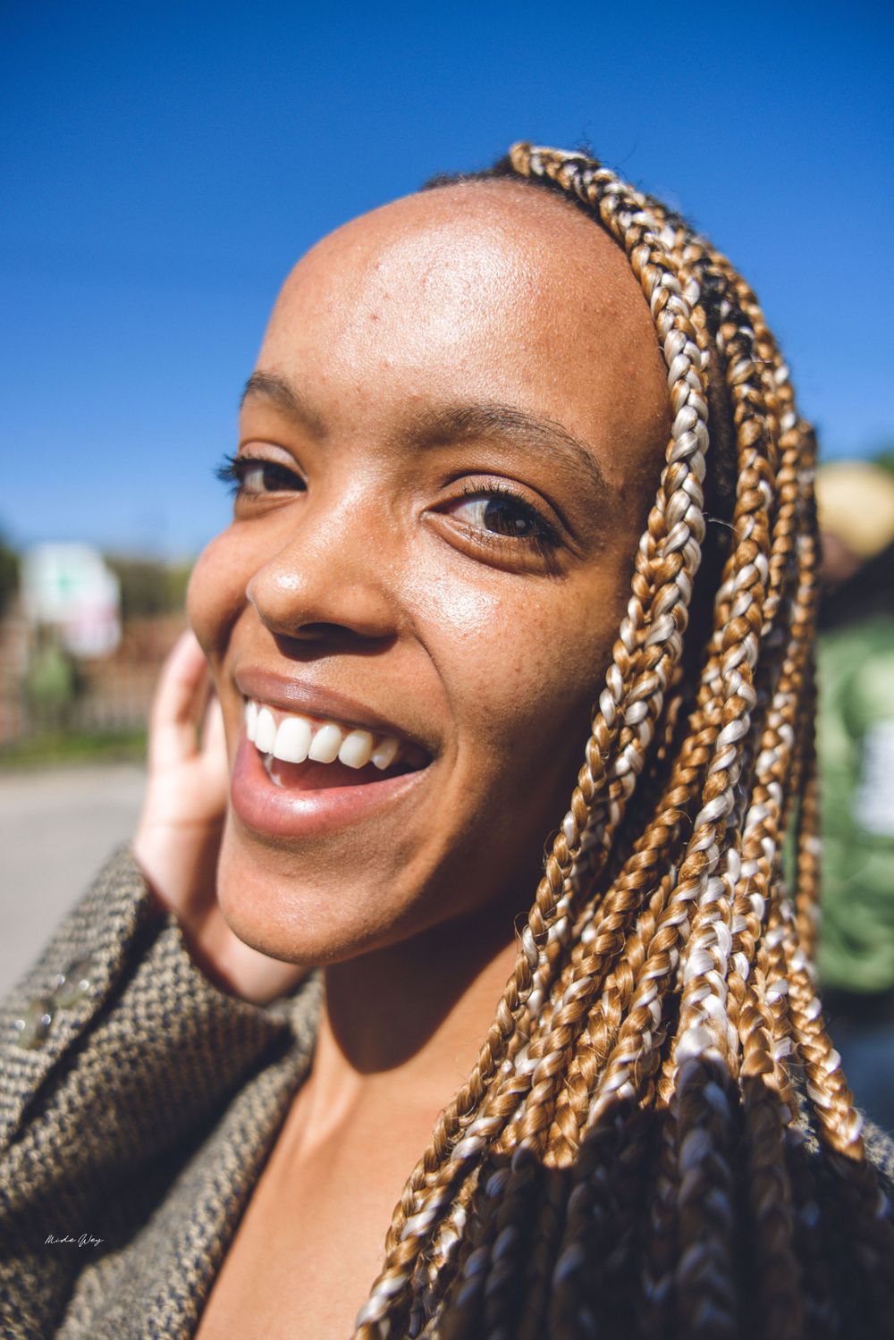 Close up portrait of someone with blonde braids smiling warmly in natural sunlight.