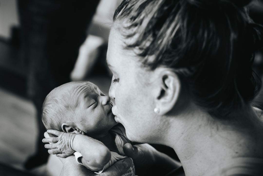 BW image of a newborn twin puckering up their lips as their mother kisses them.