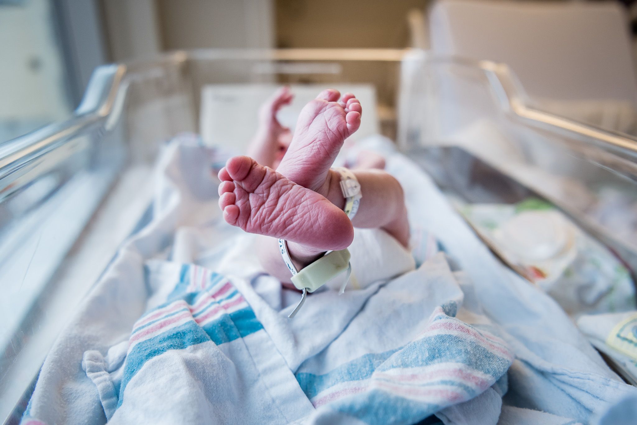 Pink baby feet kicking in the air as newborn lays in a basinet in hospital