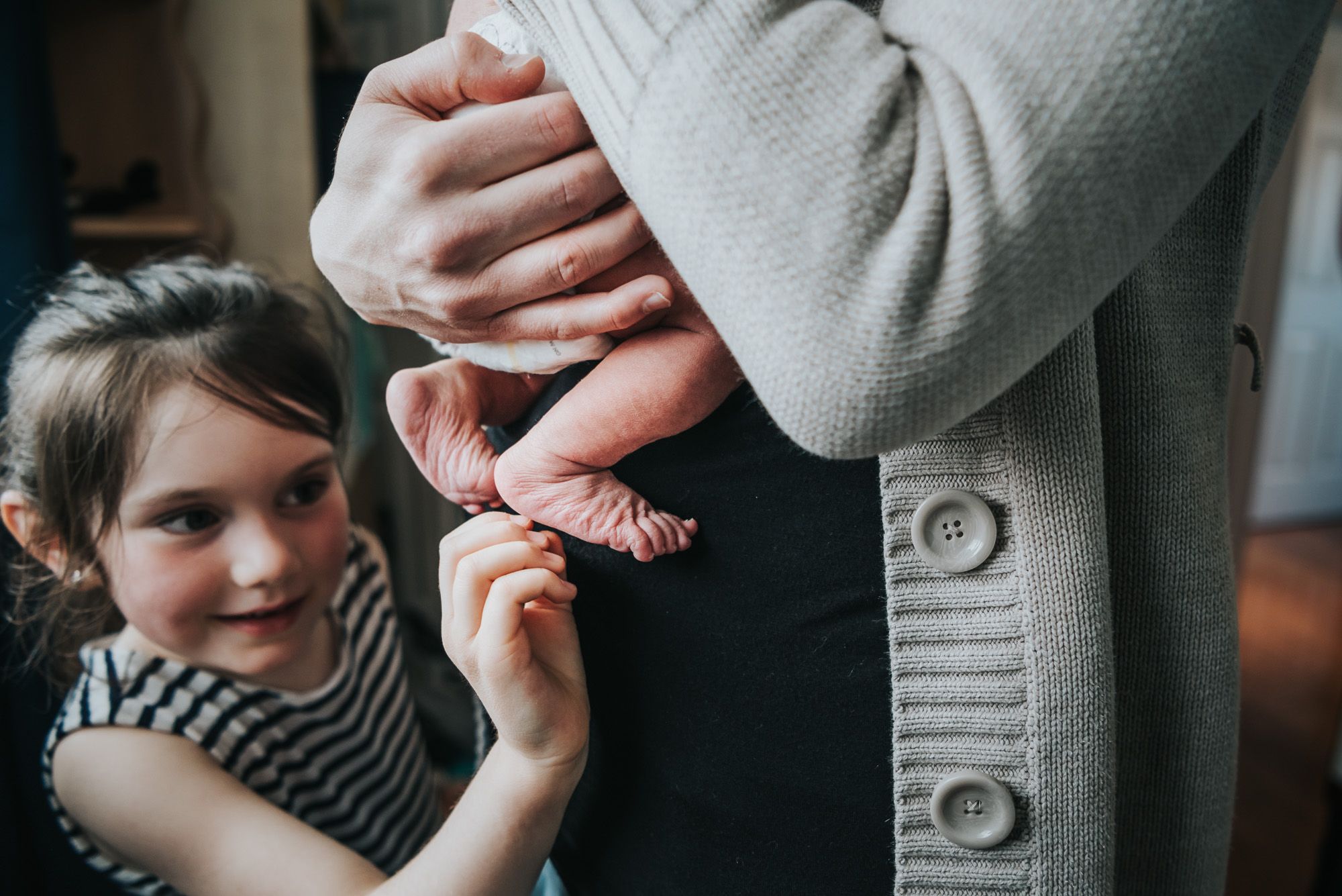 An older sister can be seen tickling her newborn sister's feet as the baby is held by her mom.