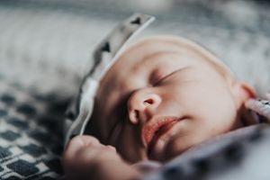 Pursed lips on a newborn stand out in this image of her laying on a bed with a big bow.