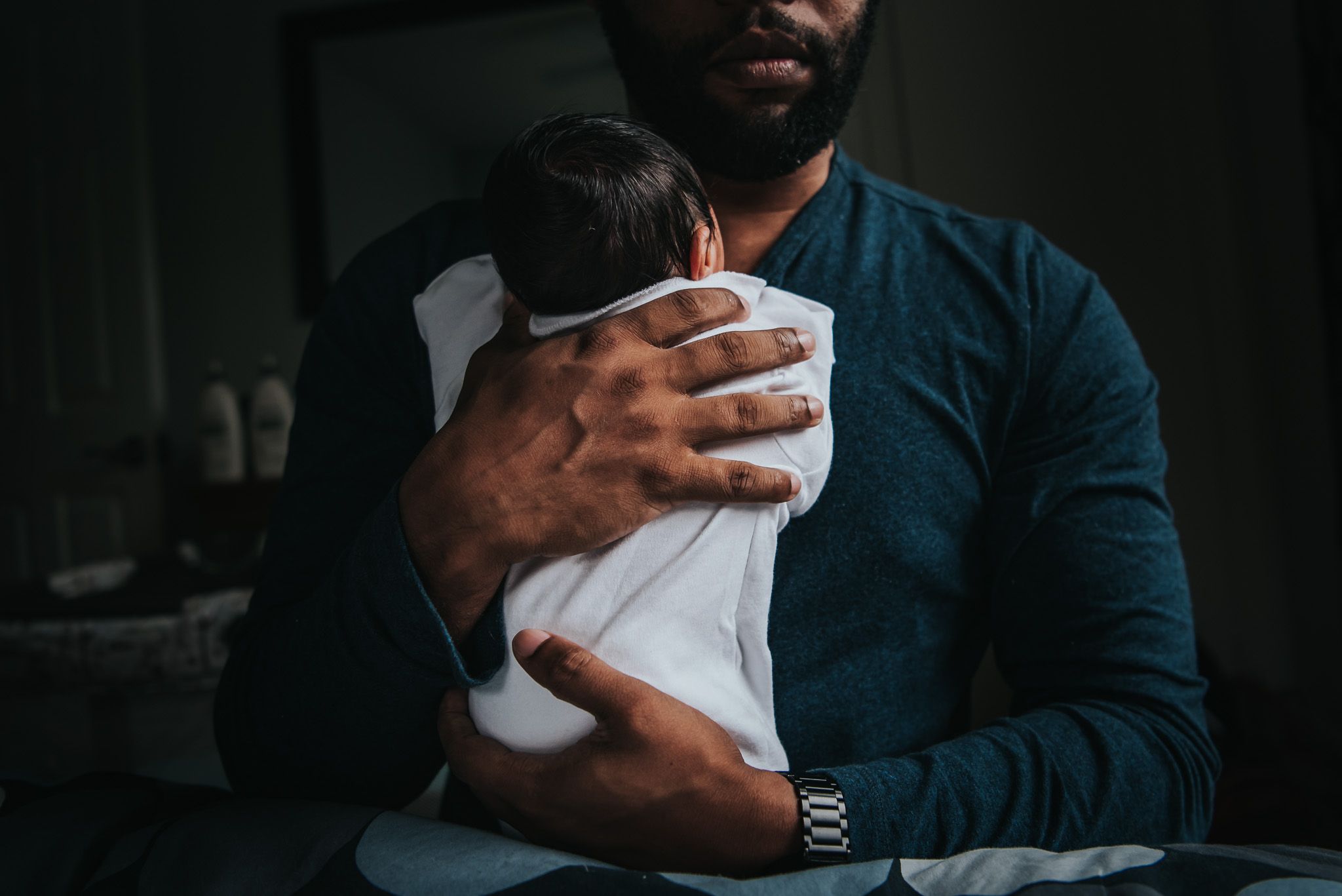 The torso of a black man holding his newborn son. You can see his strong hands holding the little baby boy.
