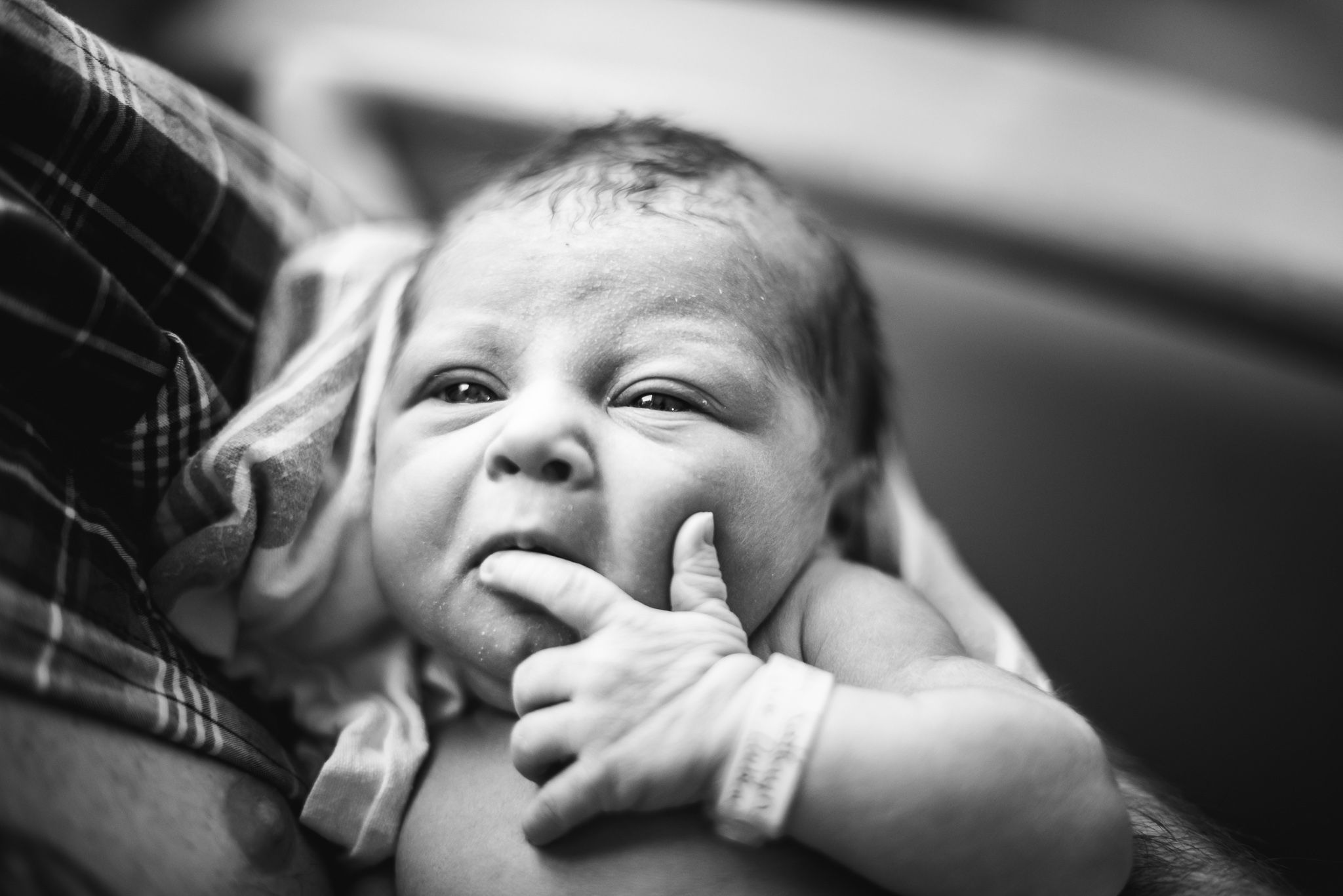 A newborn baby holds his finger to his mouth as if thinking about something important.