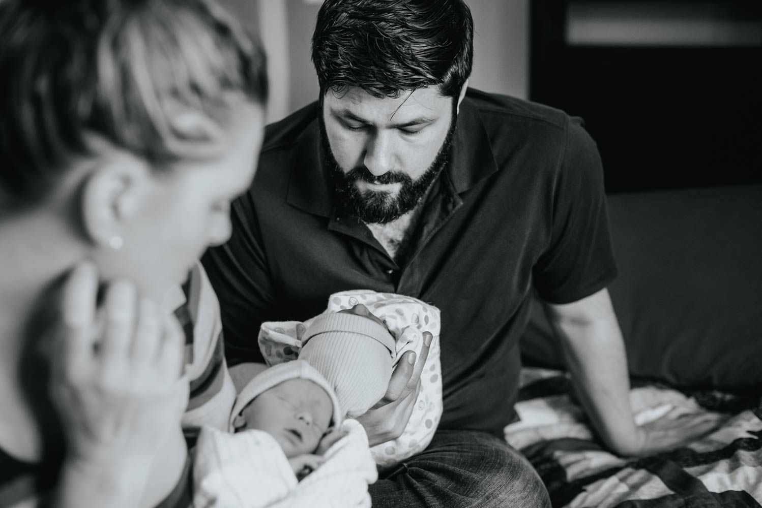 A father looks at one of his newborn twins as his wife holds the other in the foreground.