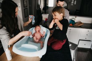 First bath for a teeny newborn on the kitchen counter with her parents and older brother all helping out.