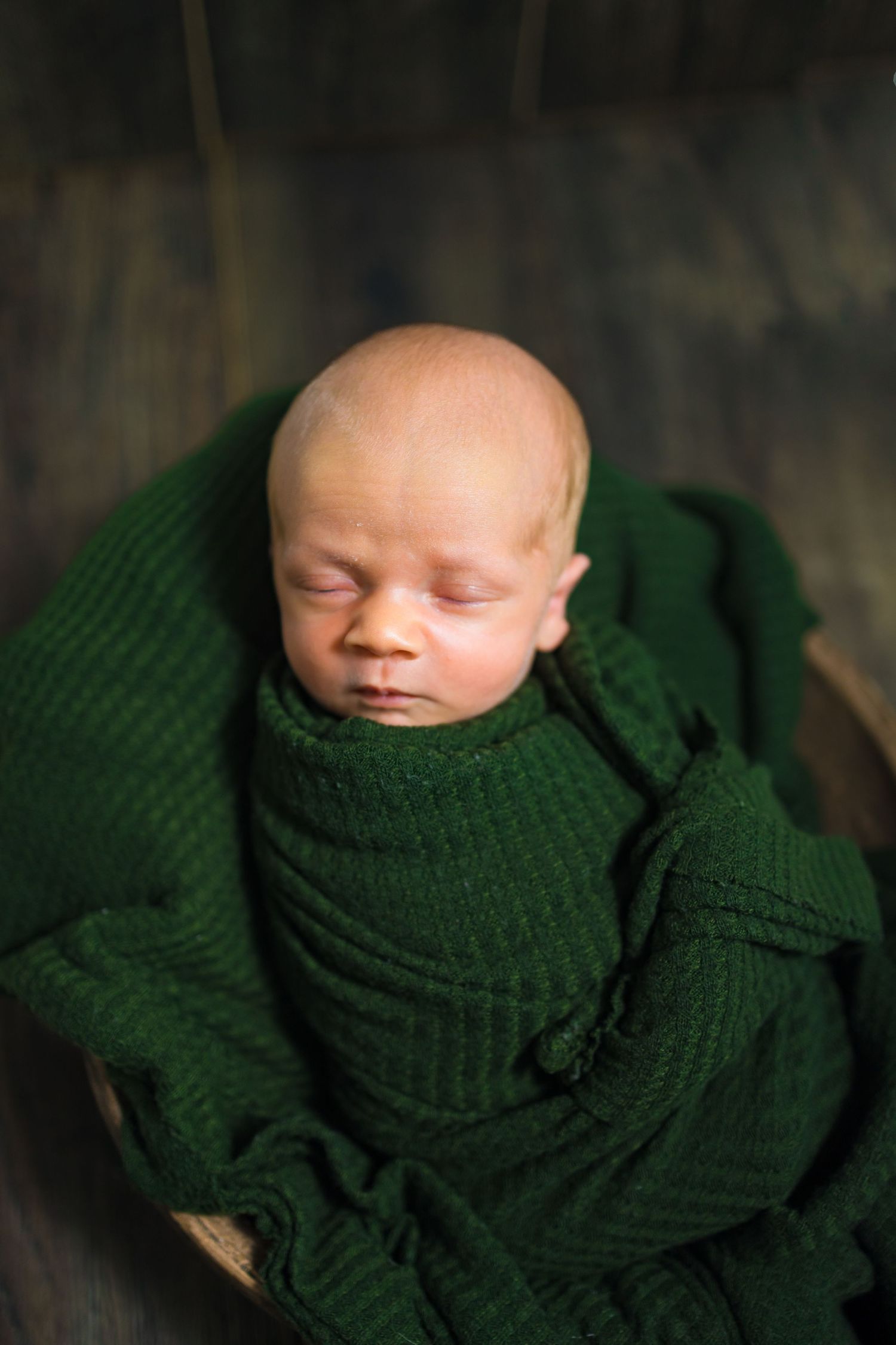 Sleeping newborn baby wrapped in green knit blanket.
