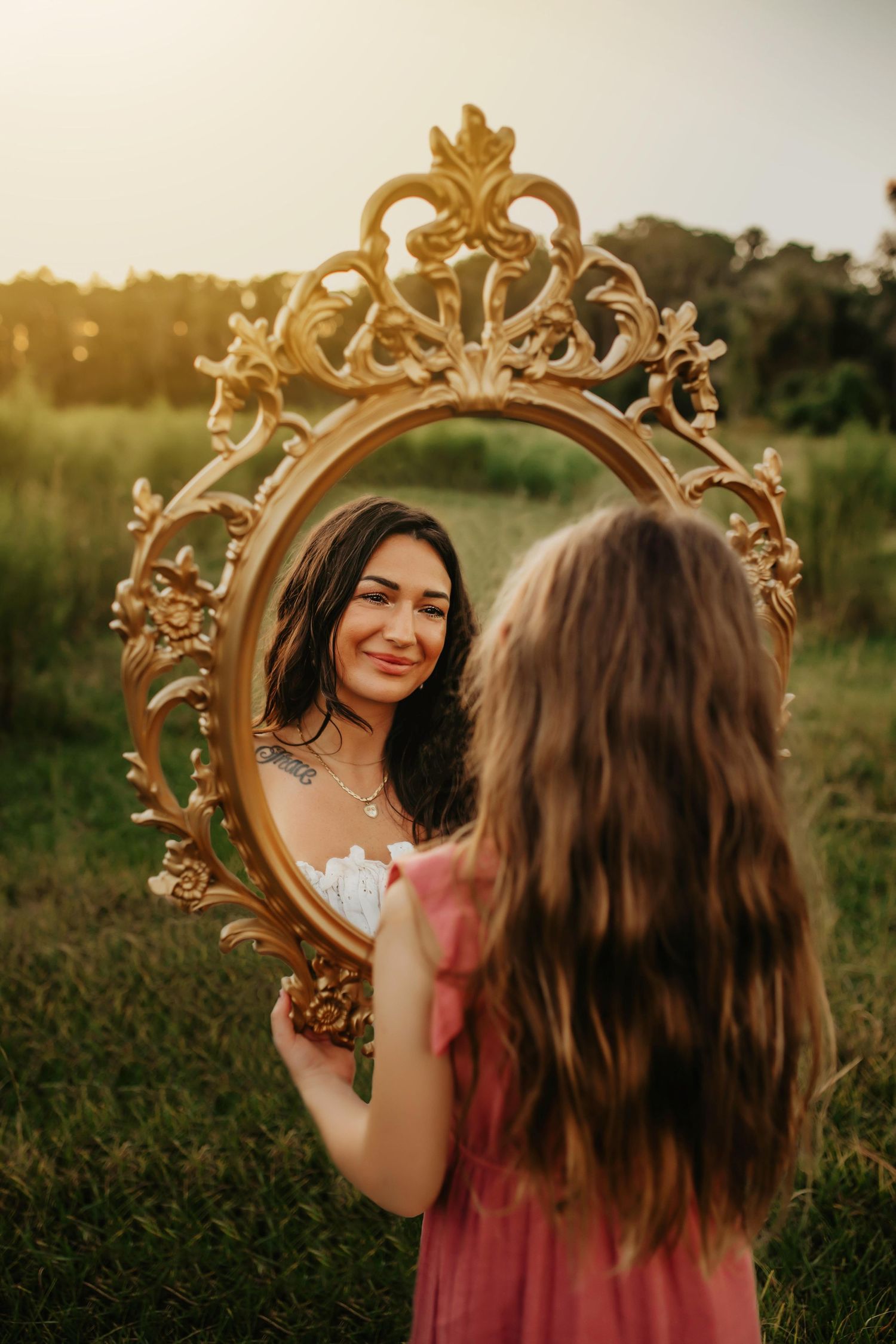 Creative outdoor portrait using an ornate gold vintage mirror frame in a sunset field.