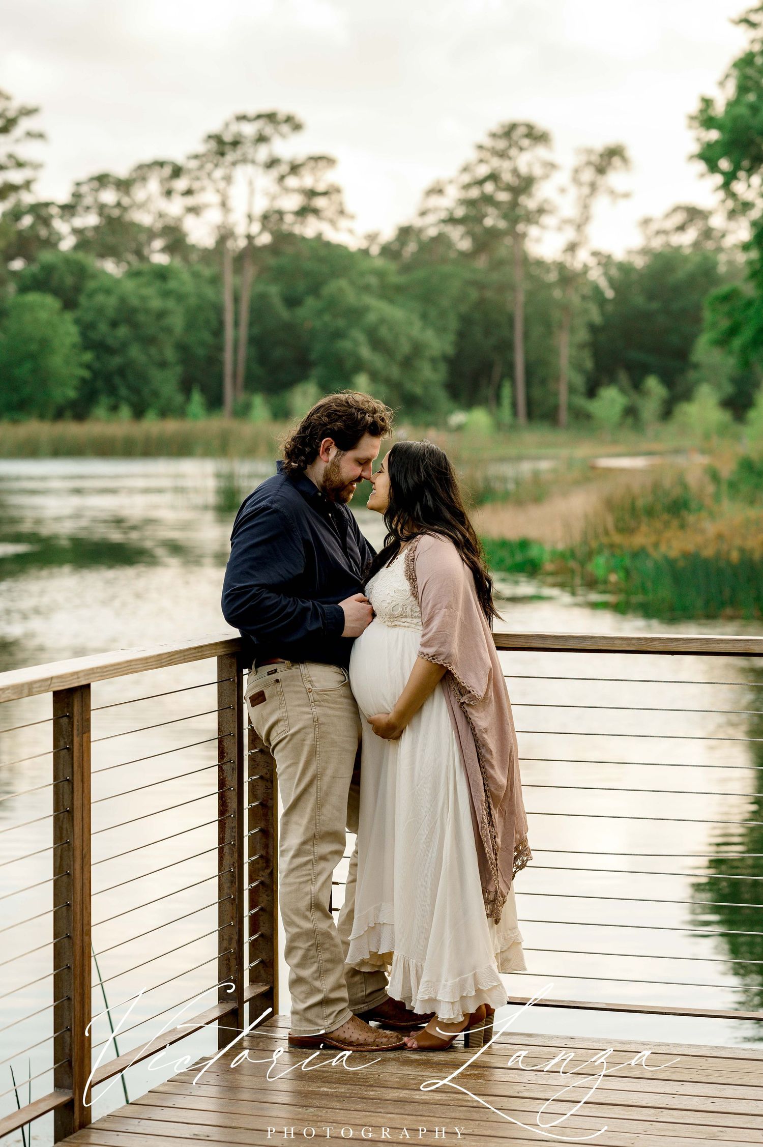 intimate maternity photo with husband embracing pregnant wife overlooking a pond and trees in houston