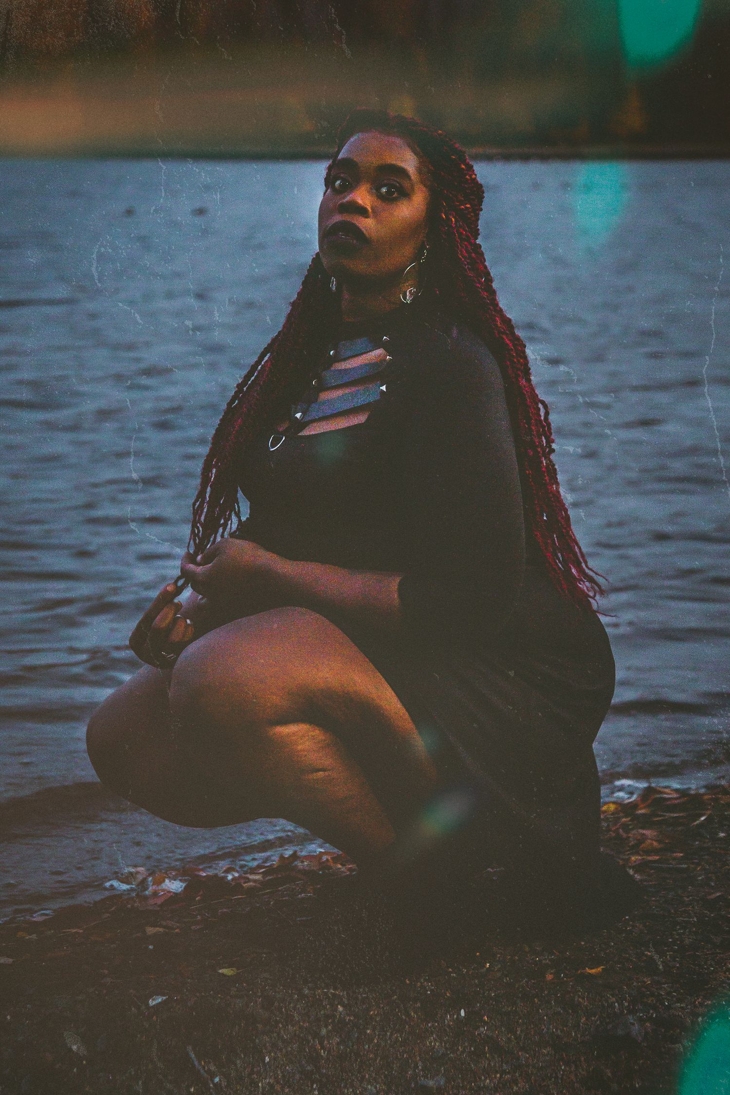 Black woman with long burgundy braids sitting by the water