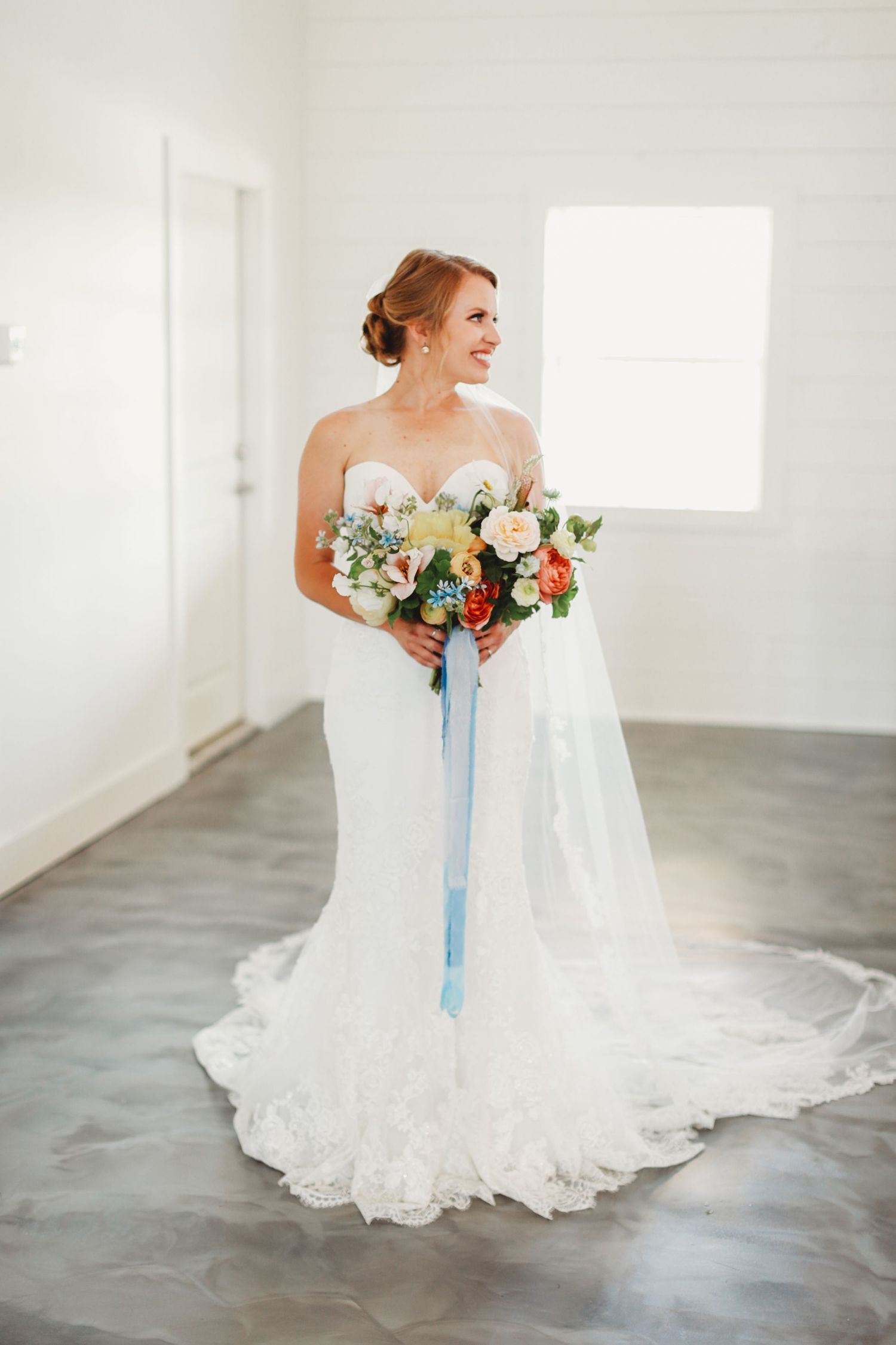 Classic bridal pose with colorful summer bouquet and flowing lace wedding gown.