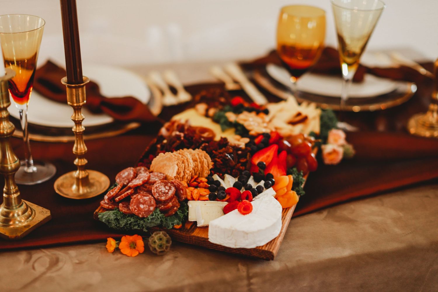 Elegant table setting with wine glasses and charcuterie board featuring meats, cheeses and fresh garnishes.