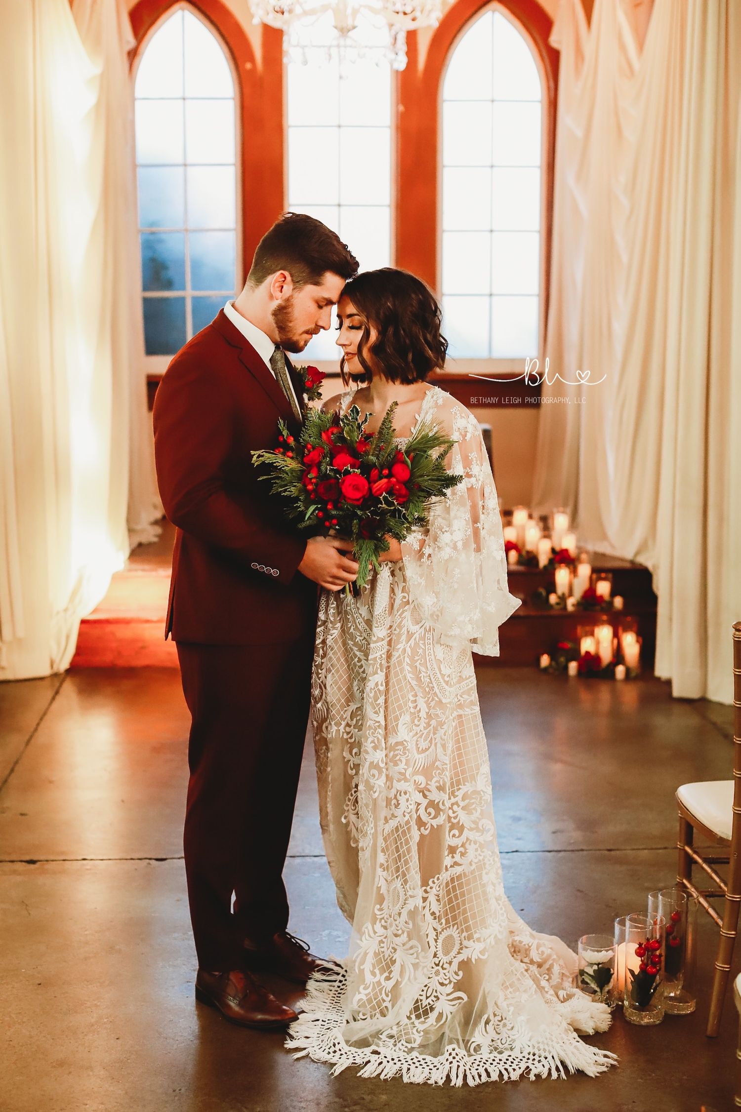 A tender wedding moment captured in a chapel with arched windows and glowing candlelight.