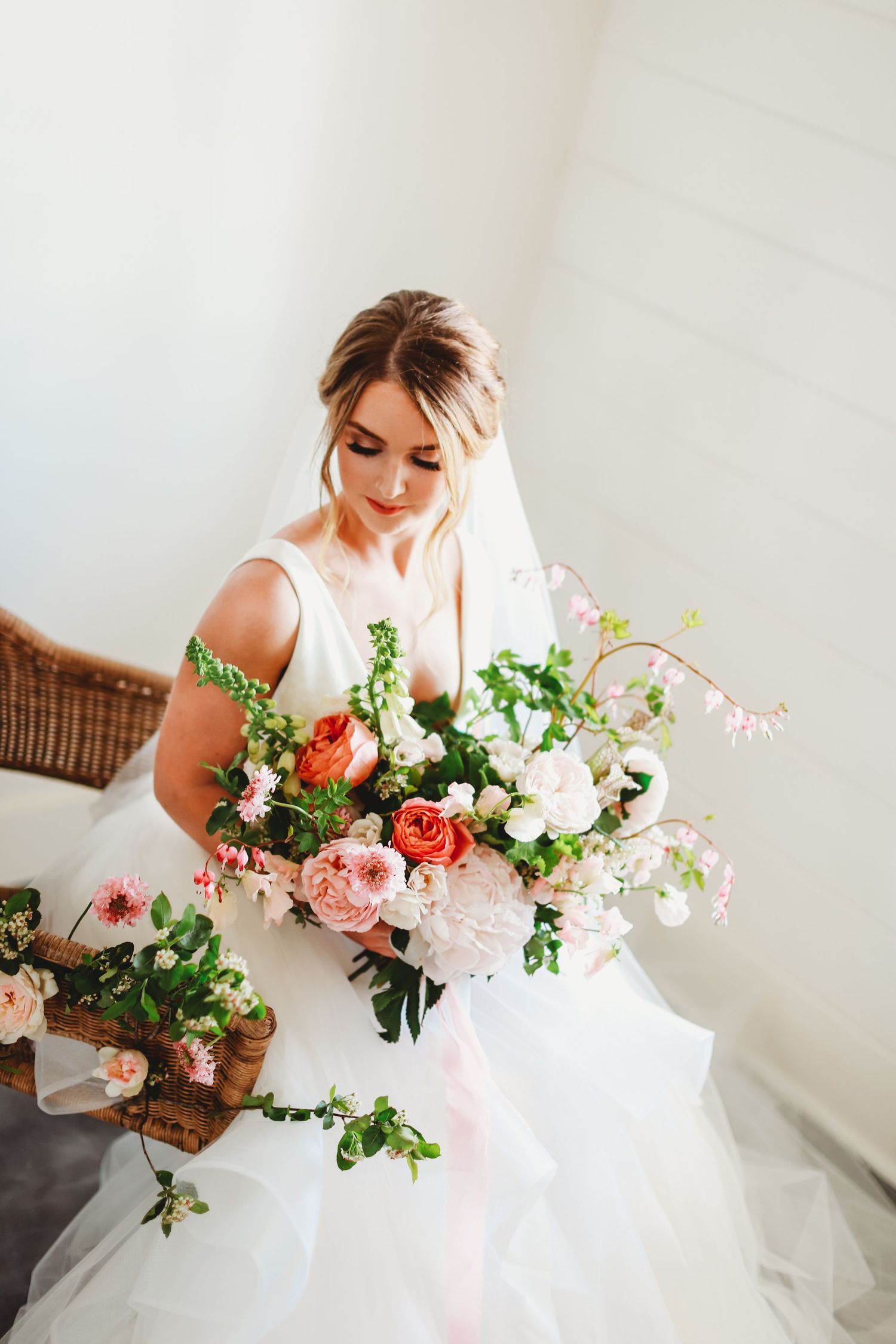 Bride in elegant white gown arranging floral bouquet in rustic setting.