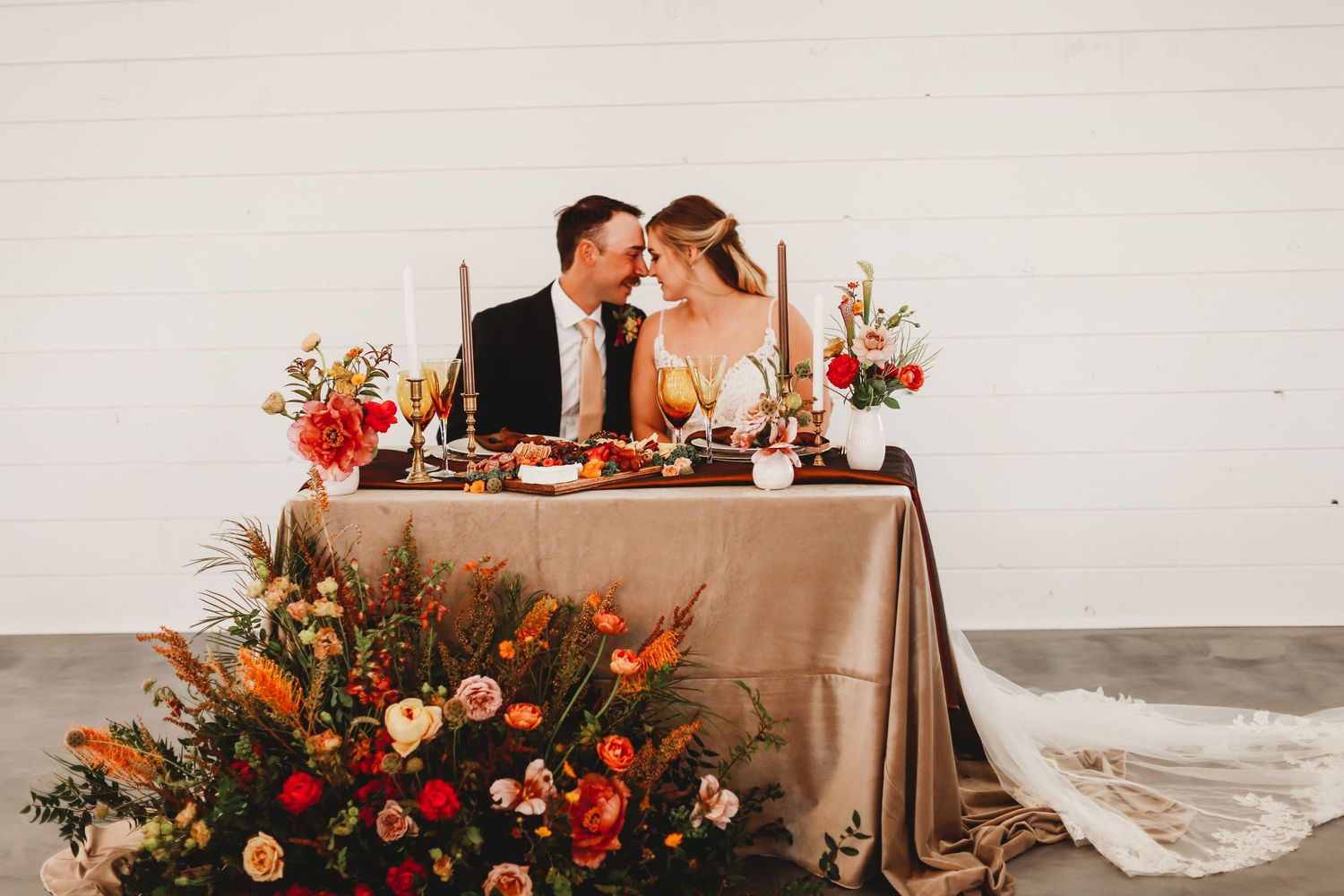Romantic table setting with warm floral arrangements and tapered candles against neutral backdrop.