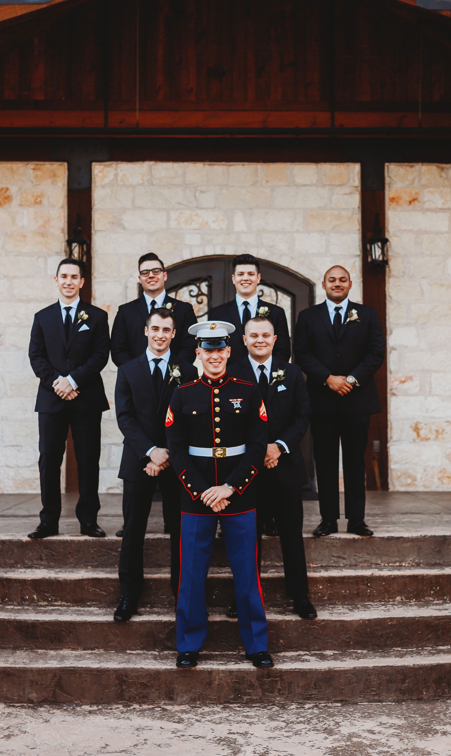 Wedding party photo featuring groomsmen in black suits with a Marine in dress blues.