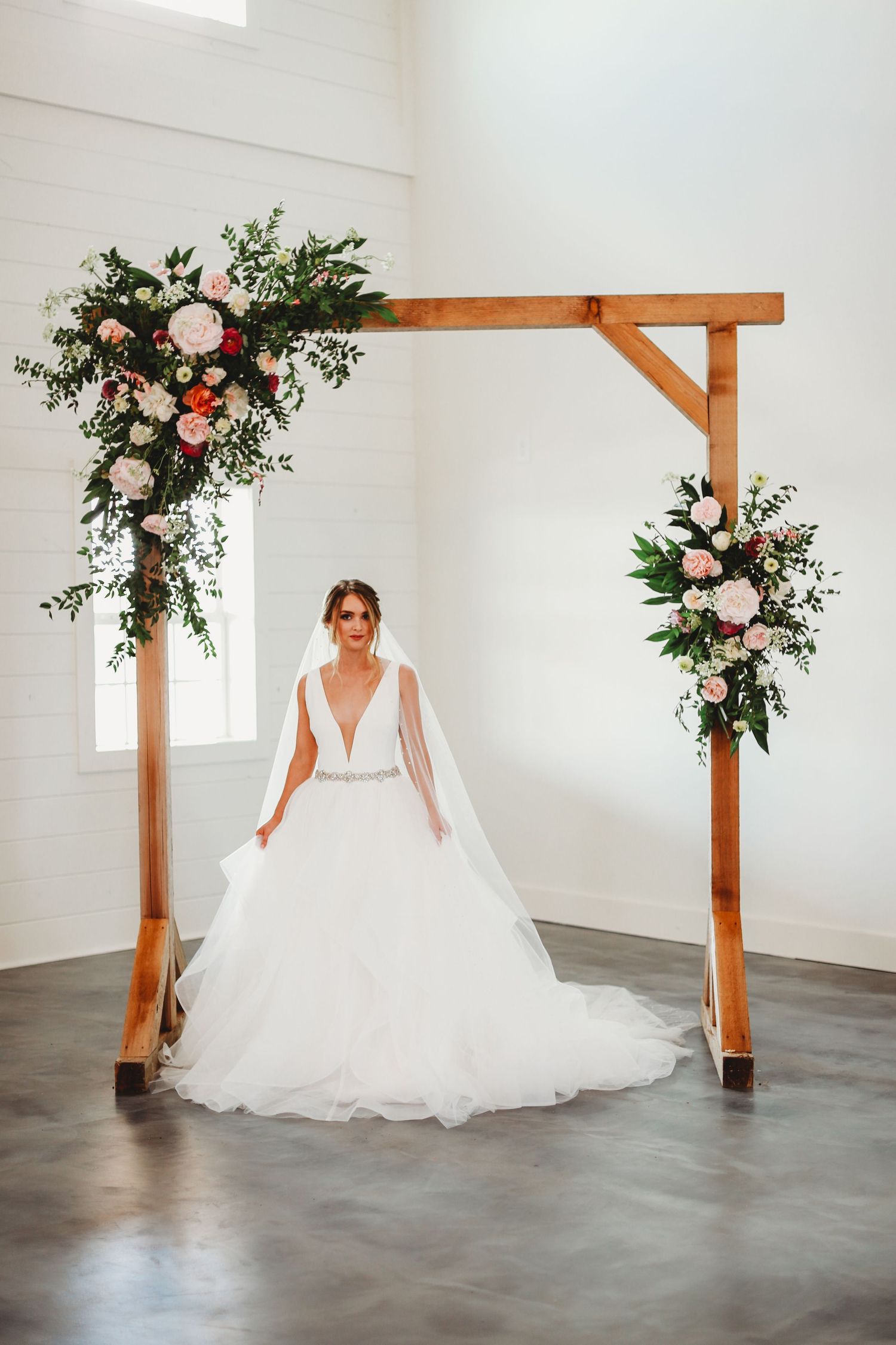 A wedding dress showcased under wooden arch decorated with pink and white floral arrangements.