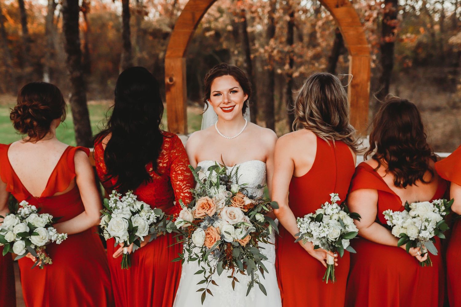 Bridal party photo showing bridesmaids in red dresses holding white floral bouquets.