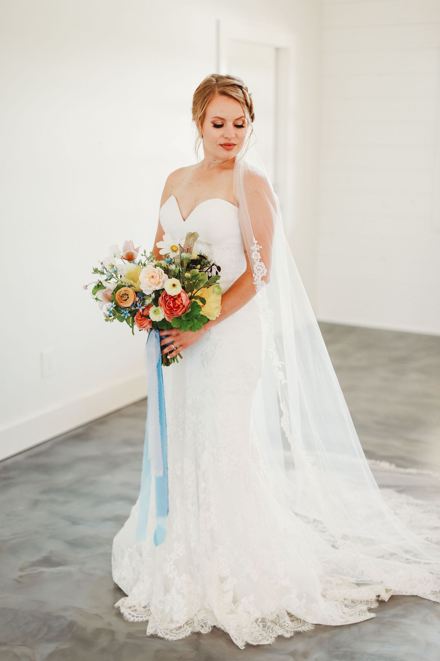 Elegant bridal portrait featuring lace wedding gown and colorful bouquet with blue ribbon.
