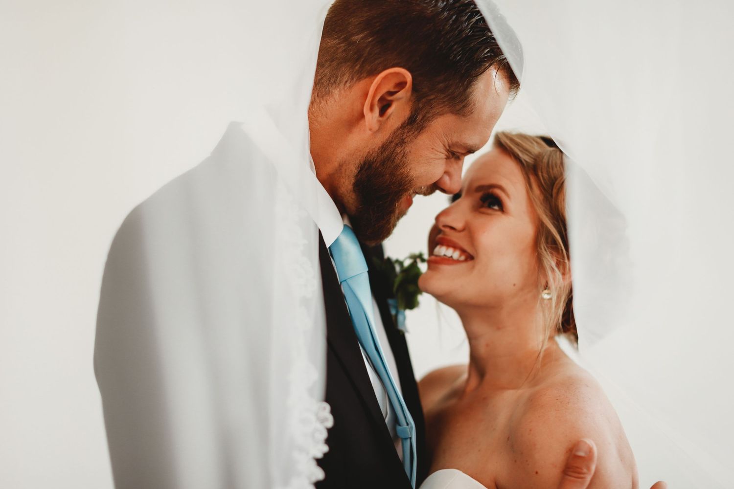 Intimate wedding moment captured in soft natural light against white wall.