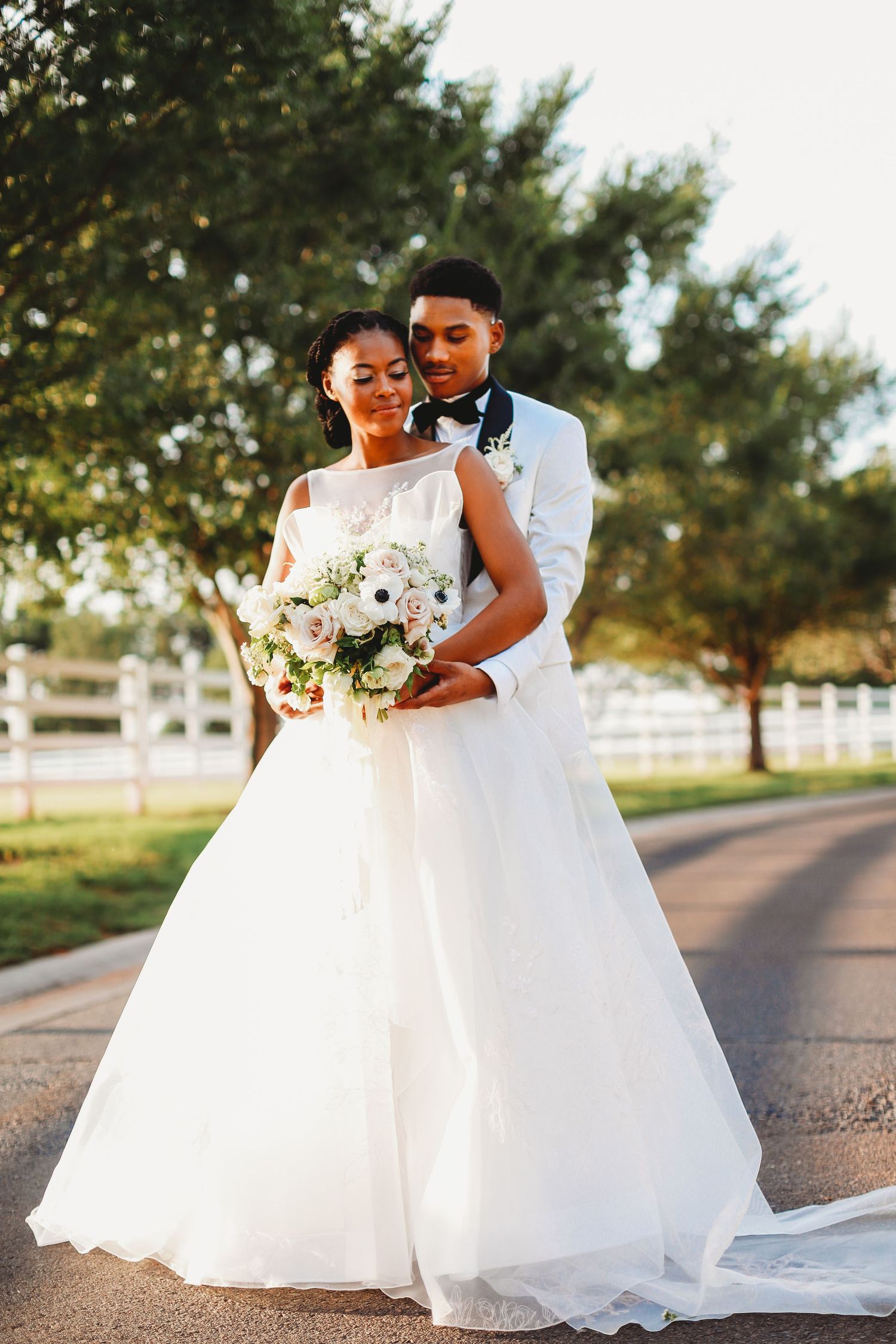 Beautiful wedding portrait with white ballgown and classic white tuxedo on a tree-lined path.