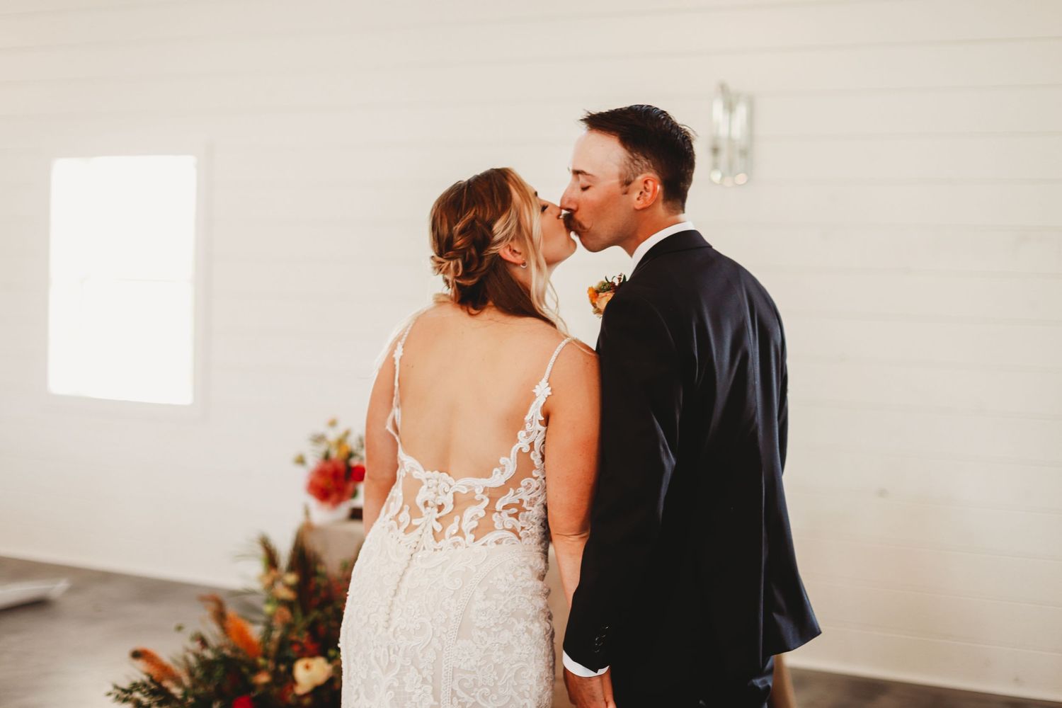 Modern wedding couple share intimate moment in front of bright window with floral decor.