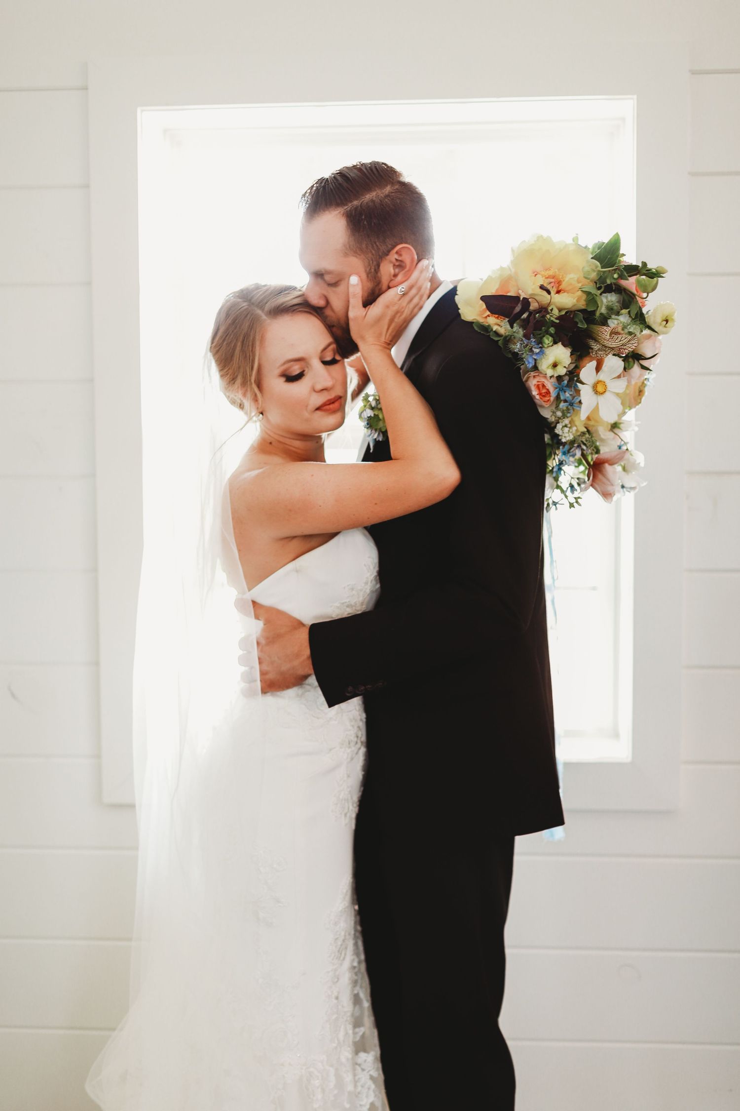 Romantic wedding portrait against bright window in minimalist white setting.