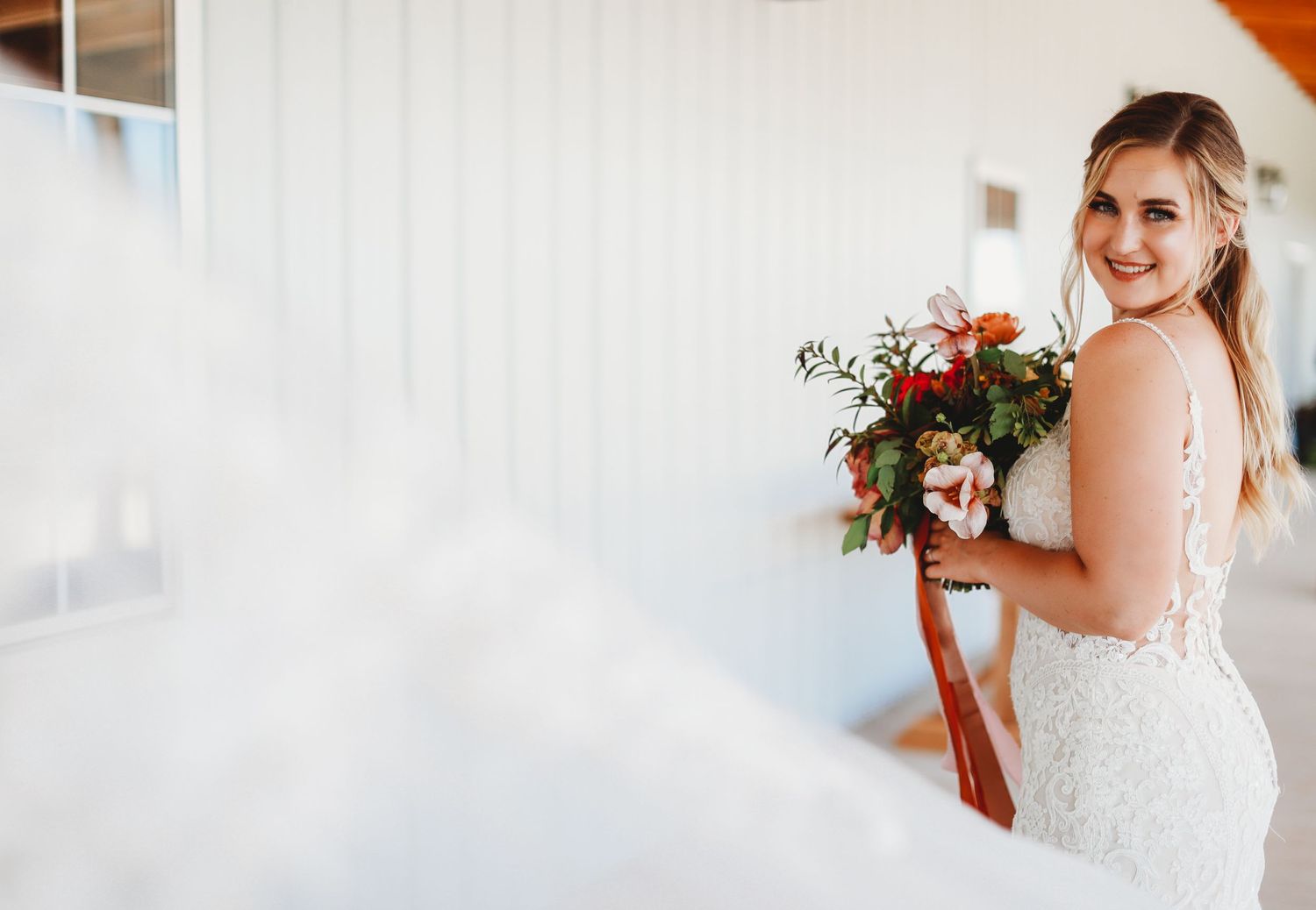 Bride in fitted lace gown holding autumn-colored bouquet.
