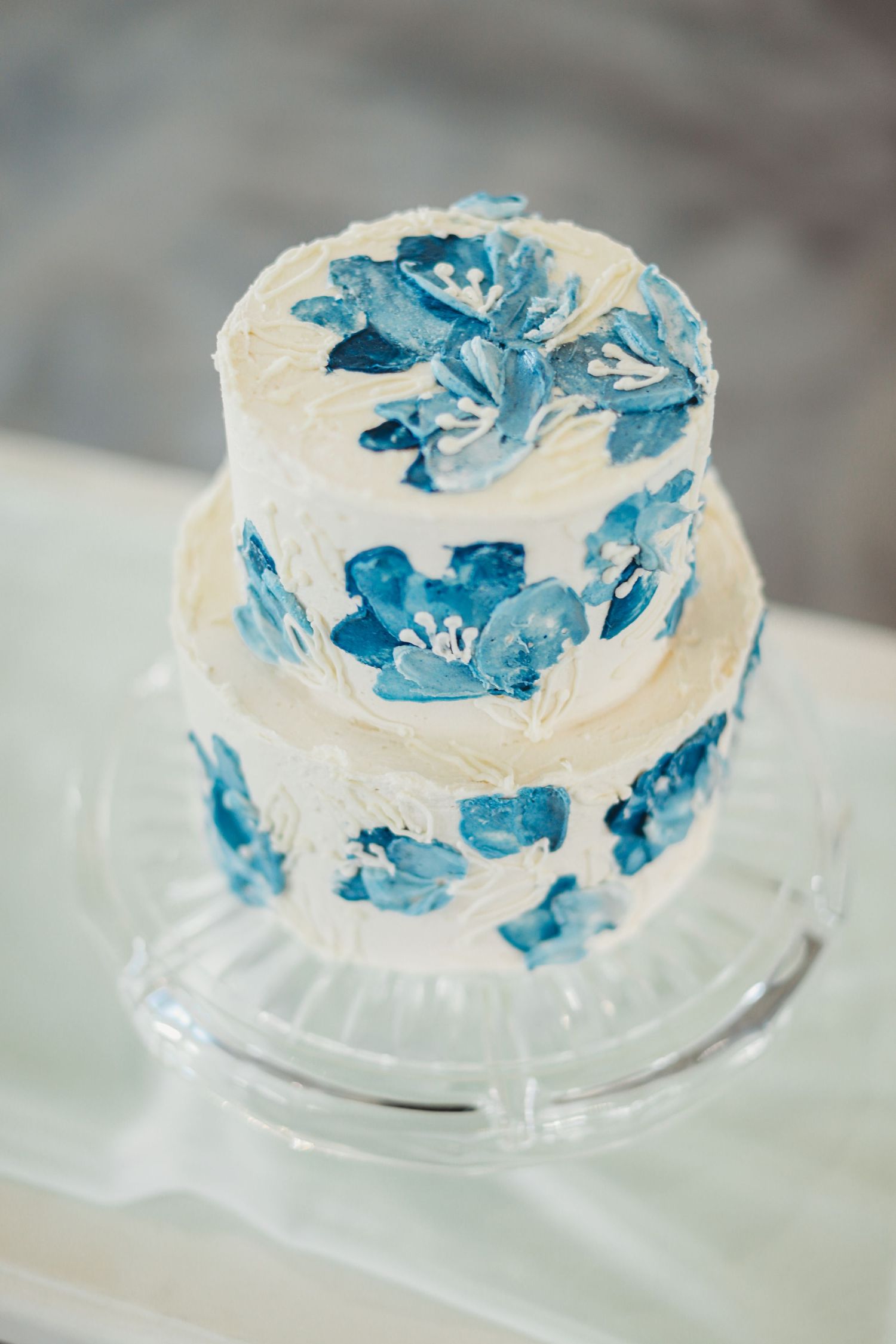 Two-tier white wedding cake decorated with hand-painted blue floral designs.