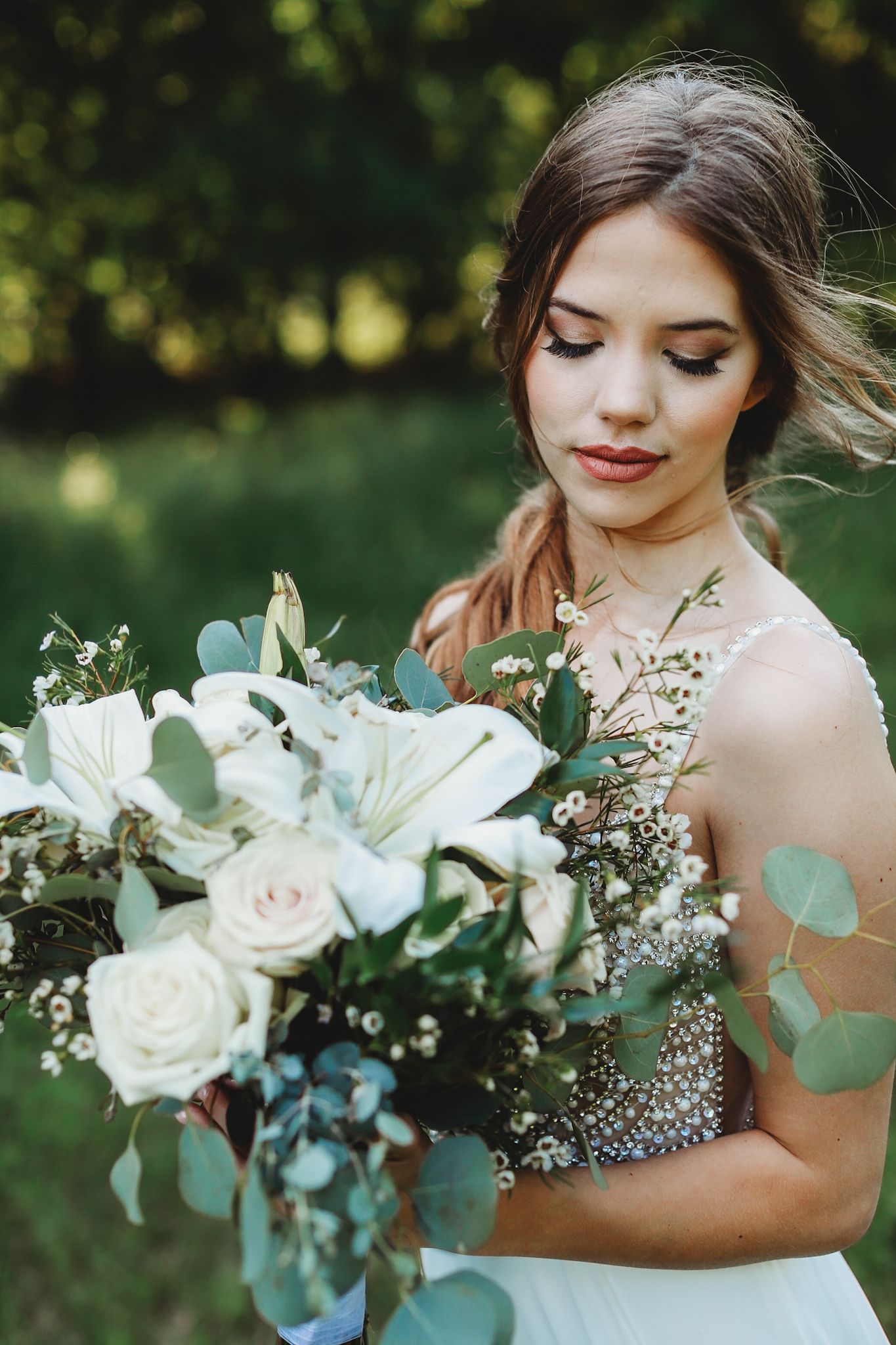 Elegant bridal portrait with white lily and rose bouquet against natural outdoor backdrop.