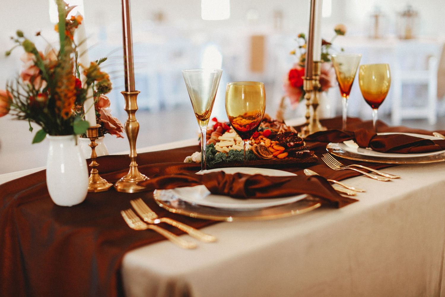 Rustic fall tablescape with burgundy linens, gold candlesticks, and wine glasses set for an elegant dinner party.