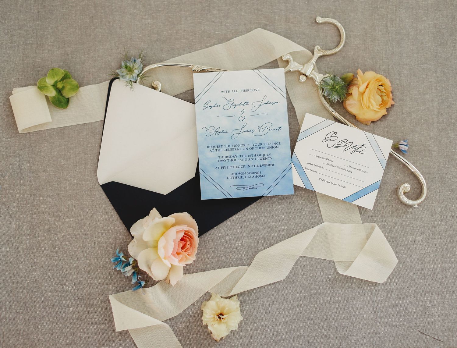 Wedding invitation suite with blue ombre design, white and peach roses, and silk ribbons on grey linen background.