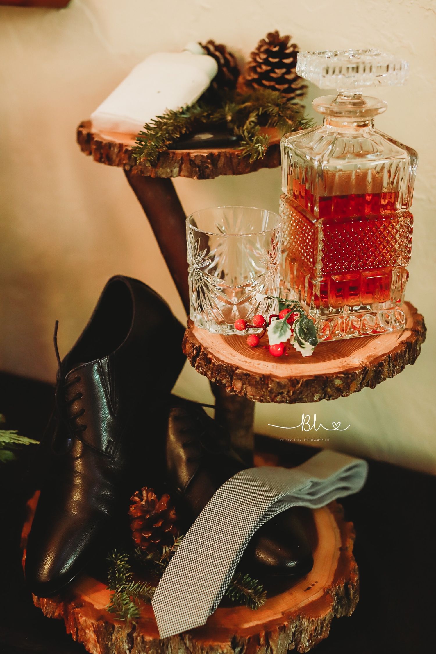 Wedding details with whiskey decanter, tie, and pinecones on rustic wood slices.