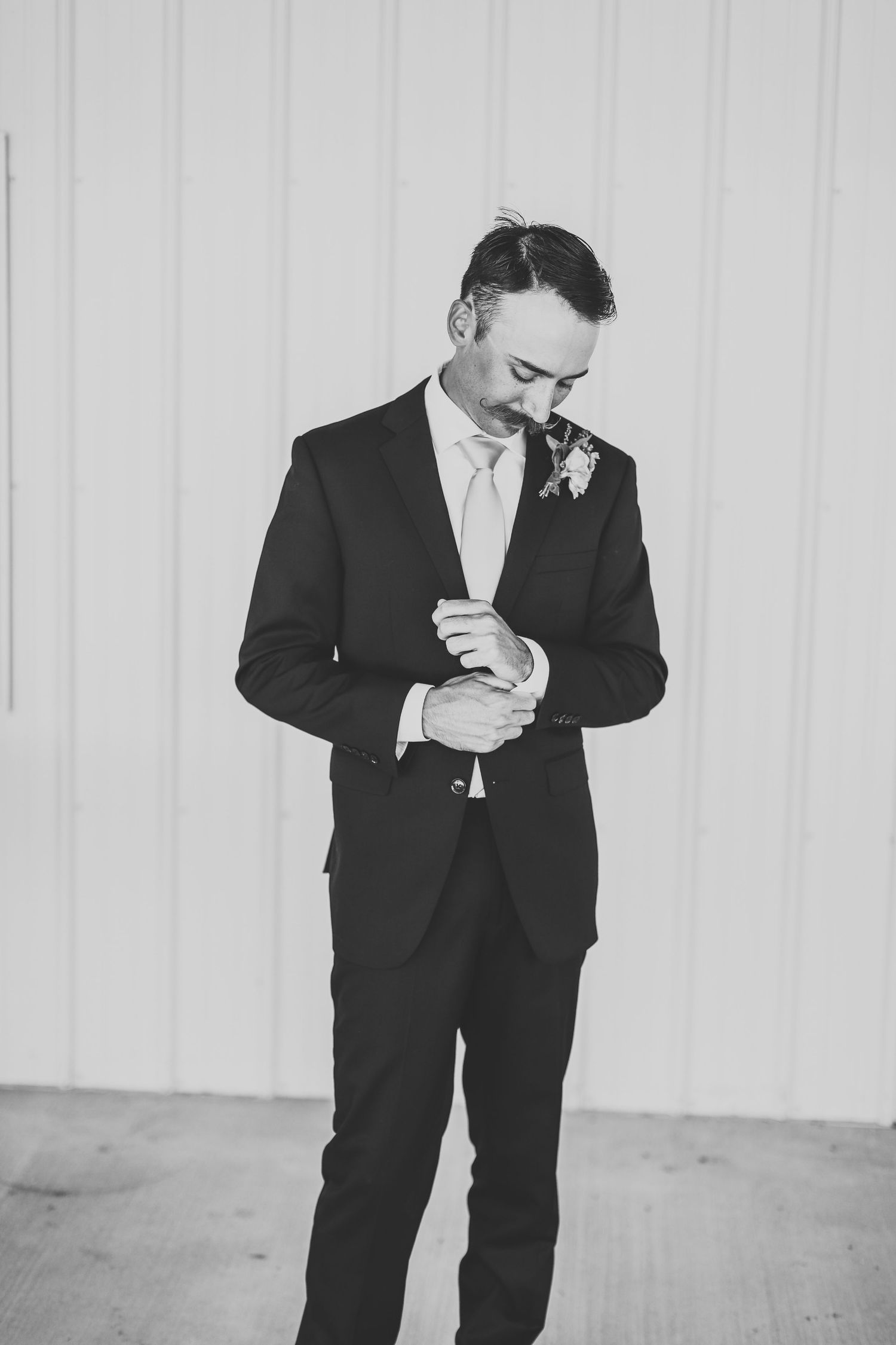 Black and white photo of a groom in a classic dark suit adjusting his cuff before the ceremony.