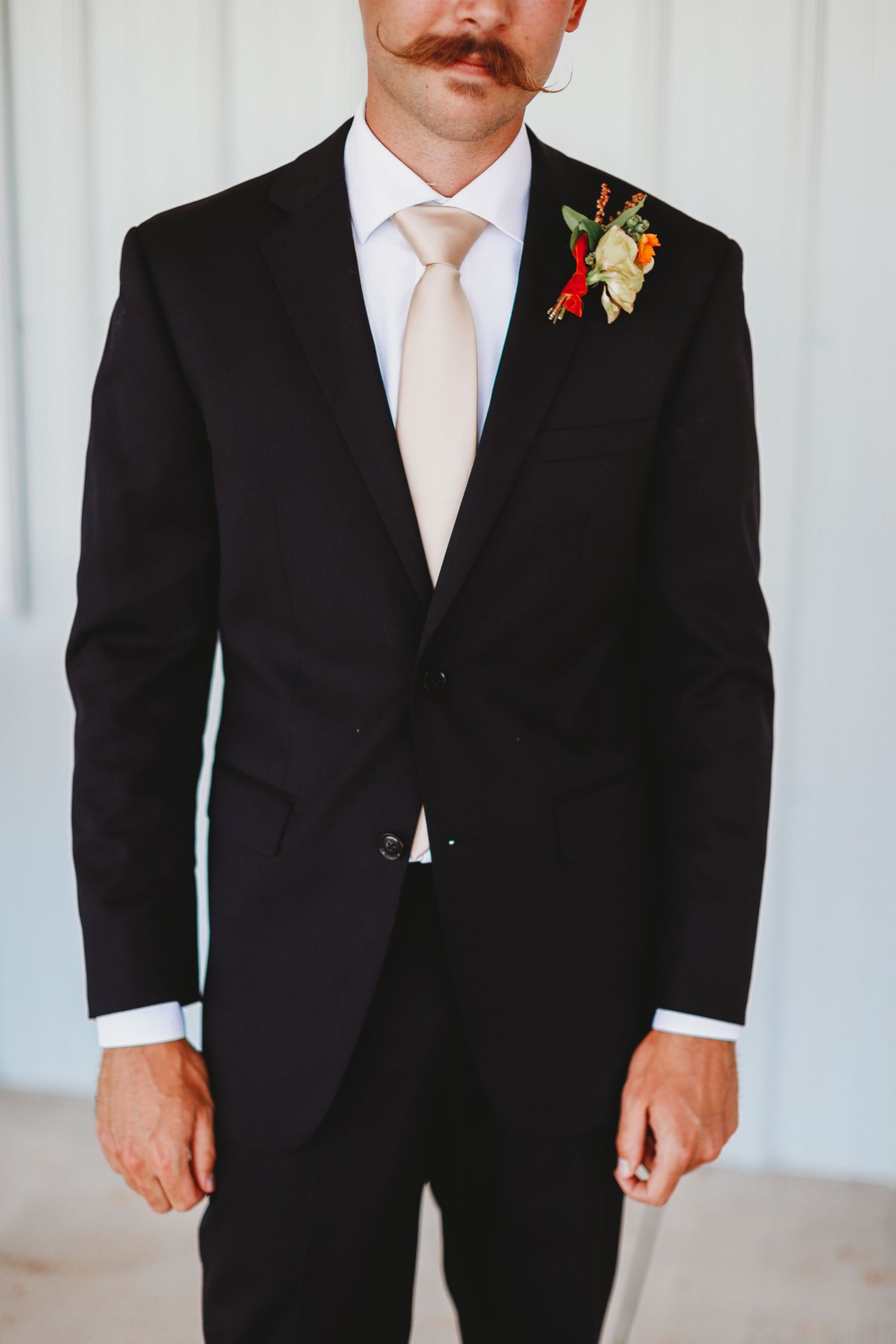 Classic groom's attire featuring black suit, peach tie and floral boutonniere.